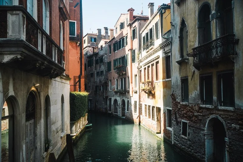 A narrow canal in Venice, Italy, lined with old colorful buildings with windows and balconies.