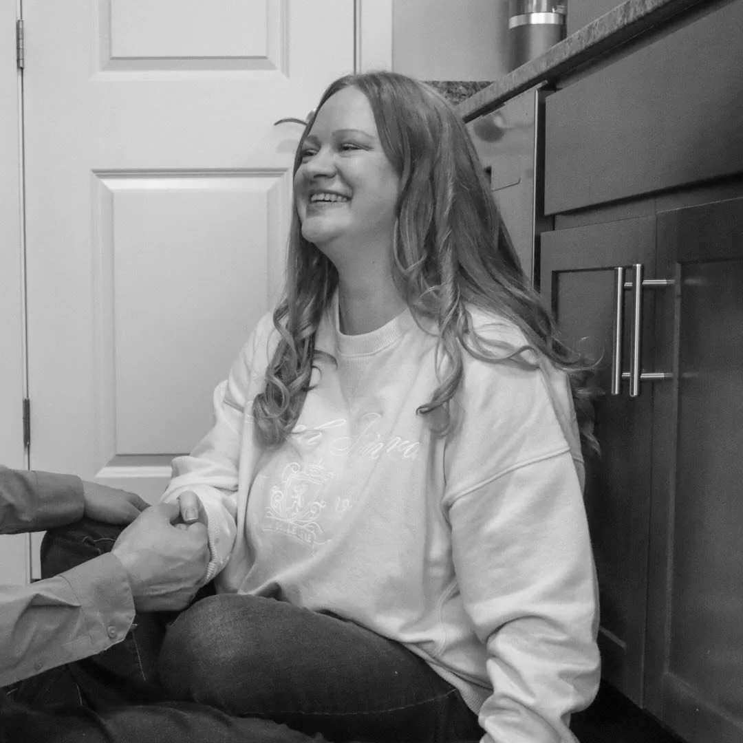 A woman smiling and sitting on the floor in a kitchen
