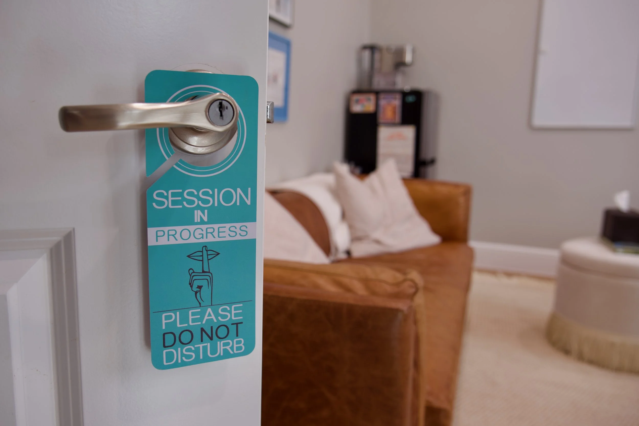 Close-up of a door with a sign that says "Session in Progress" and "Please Do Not Disturb" hanging on the door handle, with a bedroom visible in the background.