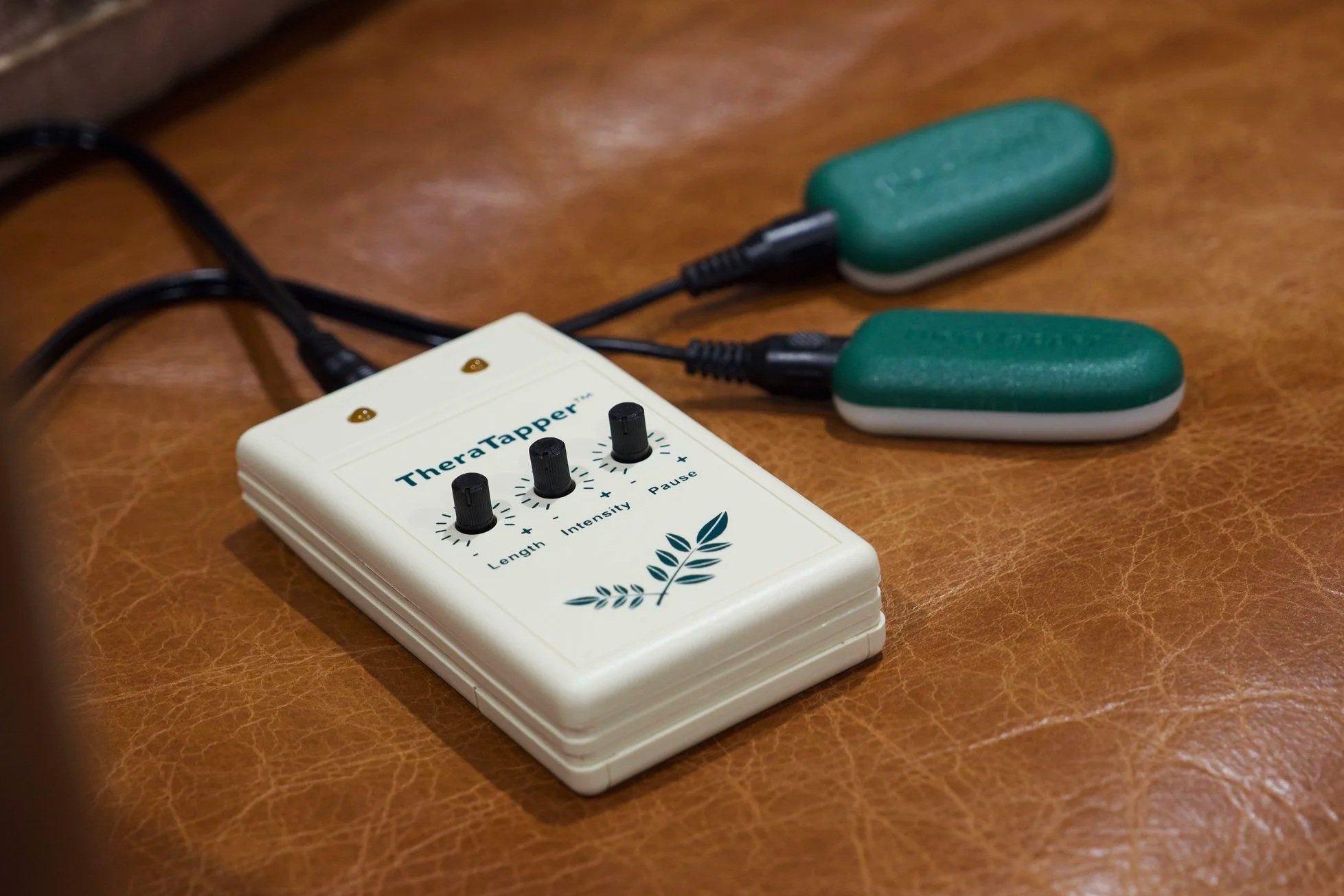 A Theratapper device with three control knobs labeled Length, Intensity, and Pause, connected to two green massage pads on a wooden surface.