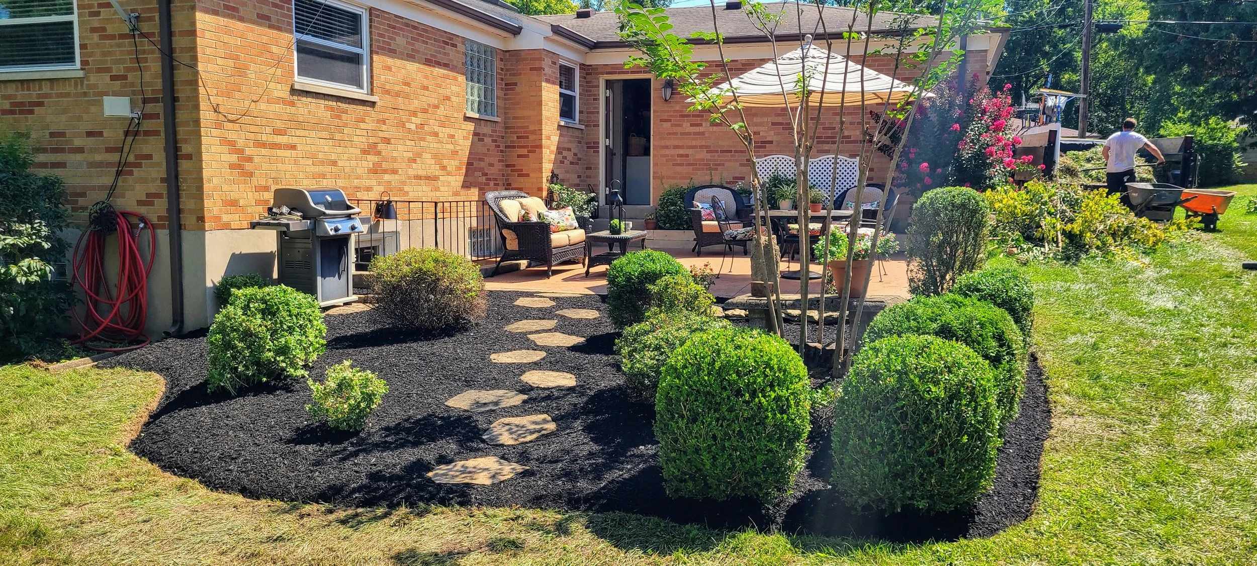 Trimmed shrubs, refreshed mulch, and maintained landscape beds around a residential patio area.