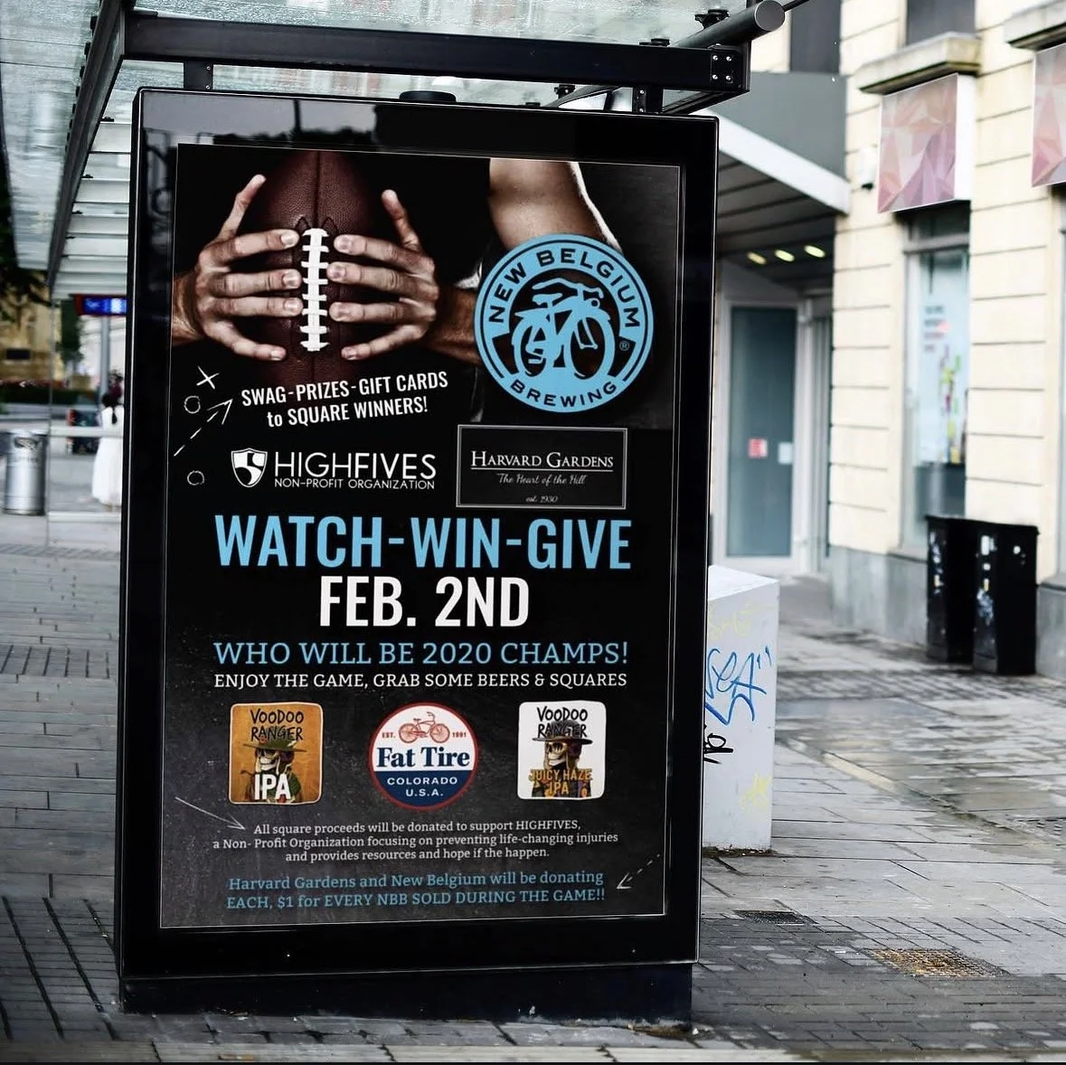 A promotional poster on a sidewalk advertising a watch-win-give event on February 2nd, supporting Highfives and featuring logos of New Belgium Brewing, Harvard Gardens, Voodoo Ranger IPA, Fat Tire Colorado, and Juicy Haze IPA. The poster has an image