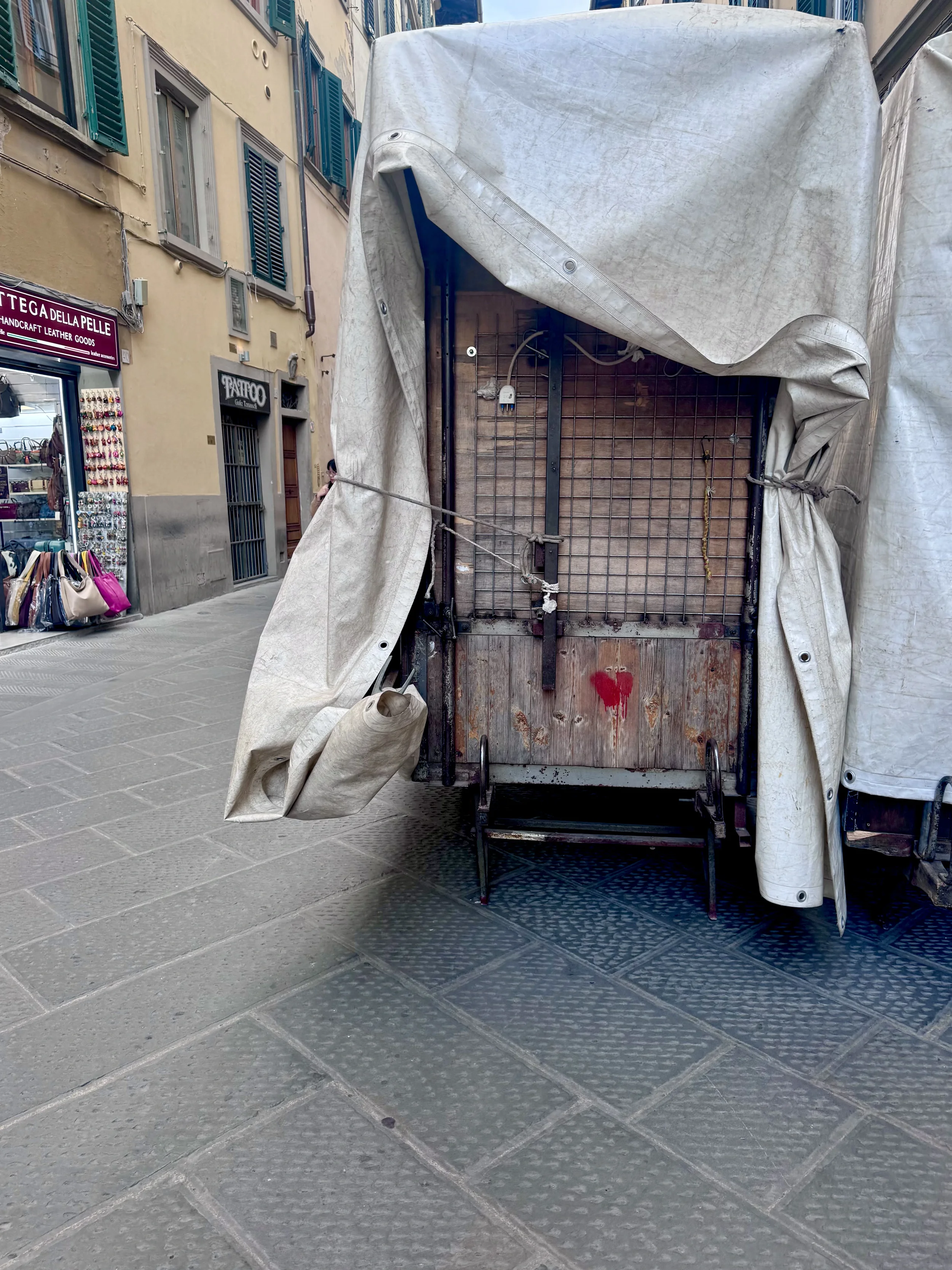 Empty vendor cart with a wooden back, partially covered with a white tarp, on a European street with shops and colorful awnings.