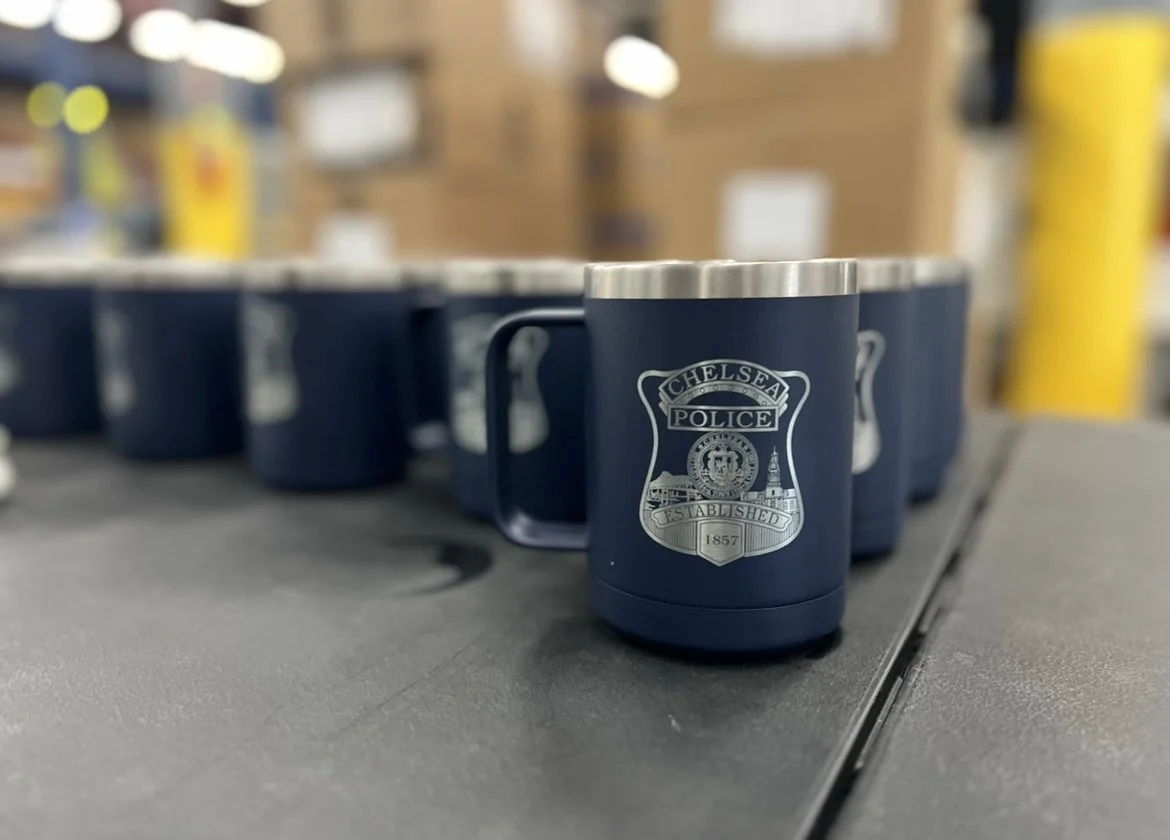 Blue Chelsea Police branded mugs with silver rims on a black table, some in the background are blurred.