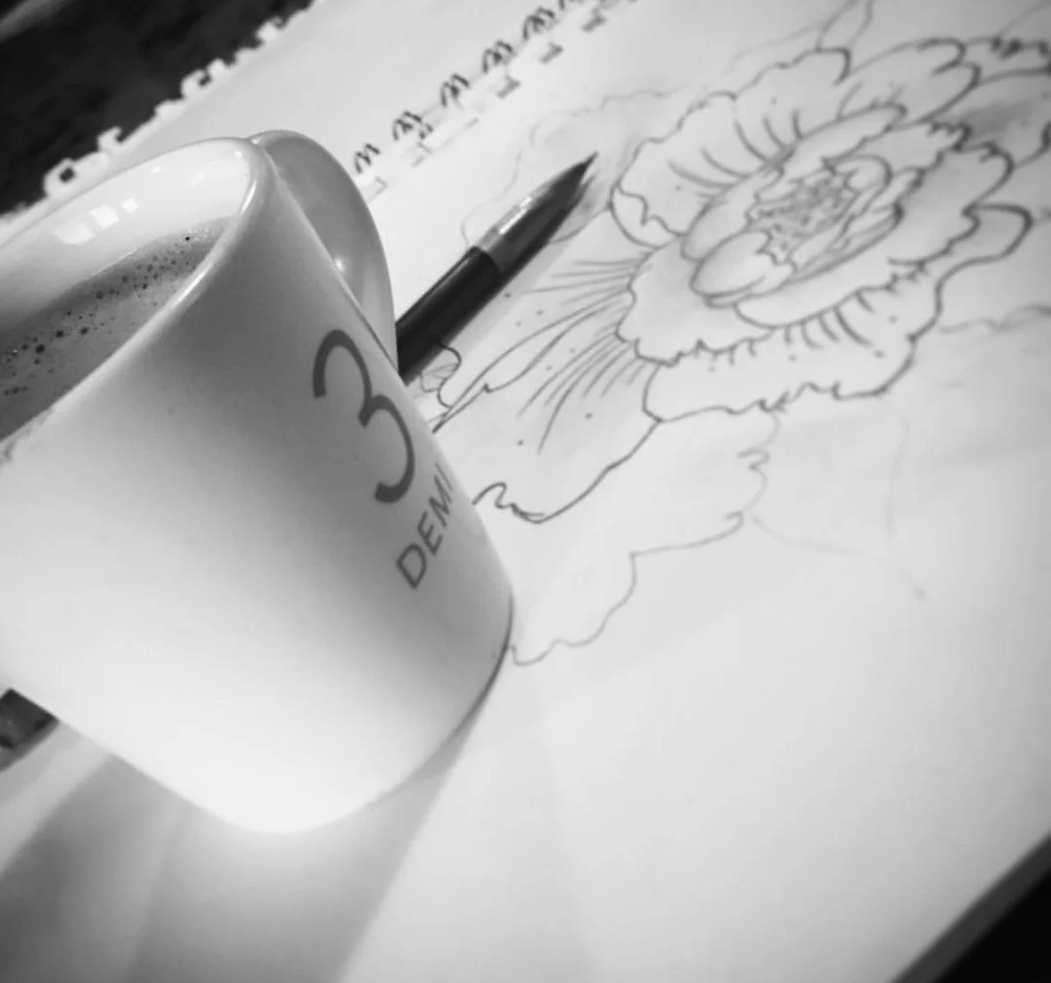A coffee mug with the number 3 on it, a pen, and a detailed floral sketch on paper in black and white.