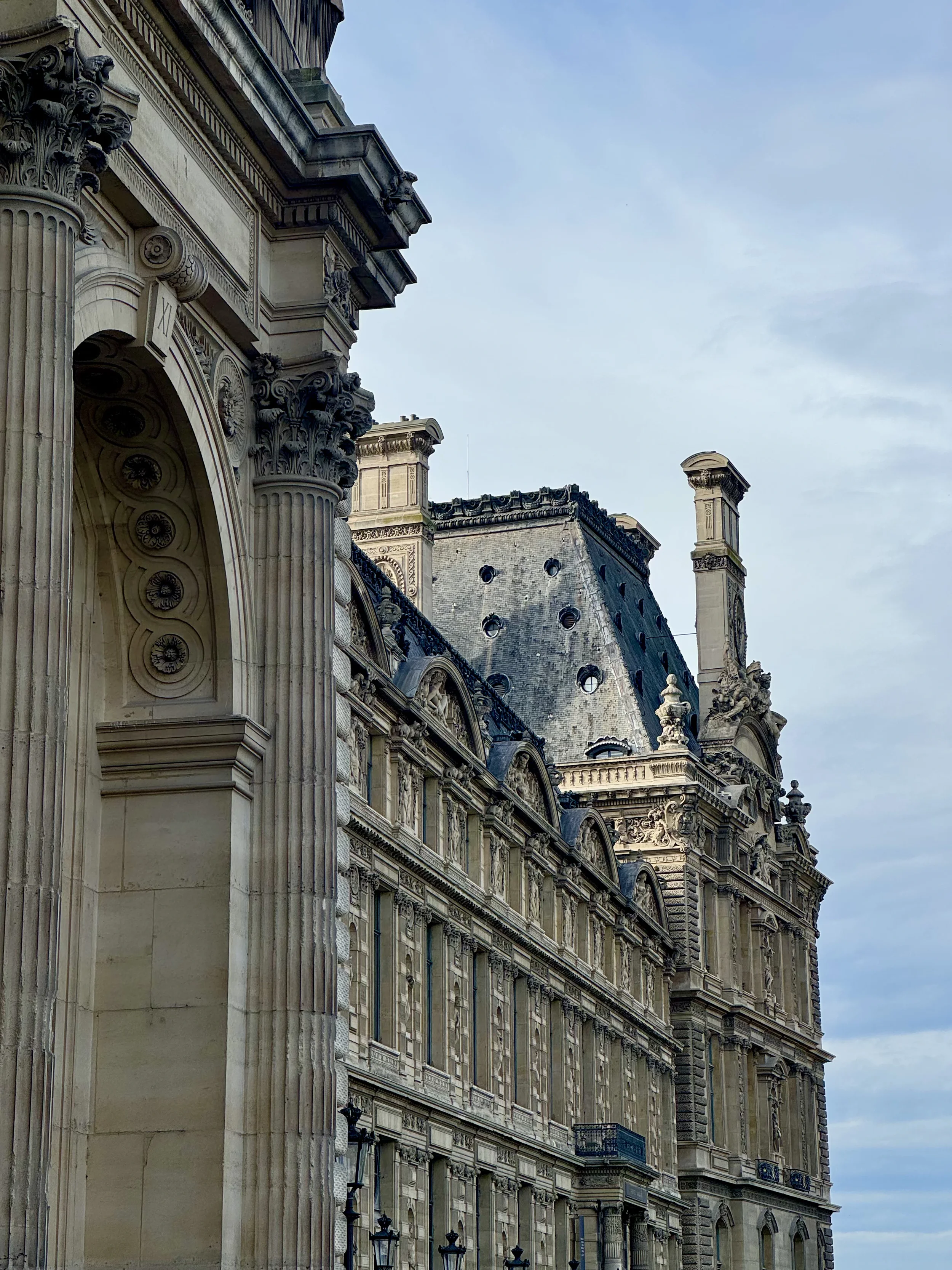 Close-up of ornate stone building with columns, decorative carvings, and a clock face, under a cloudy sky.