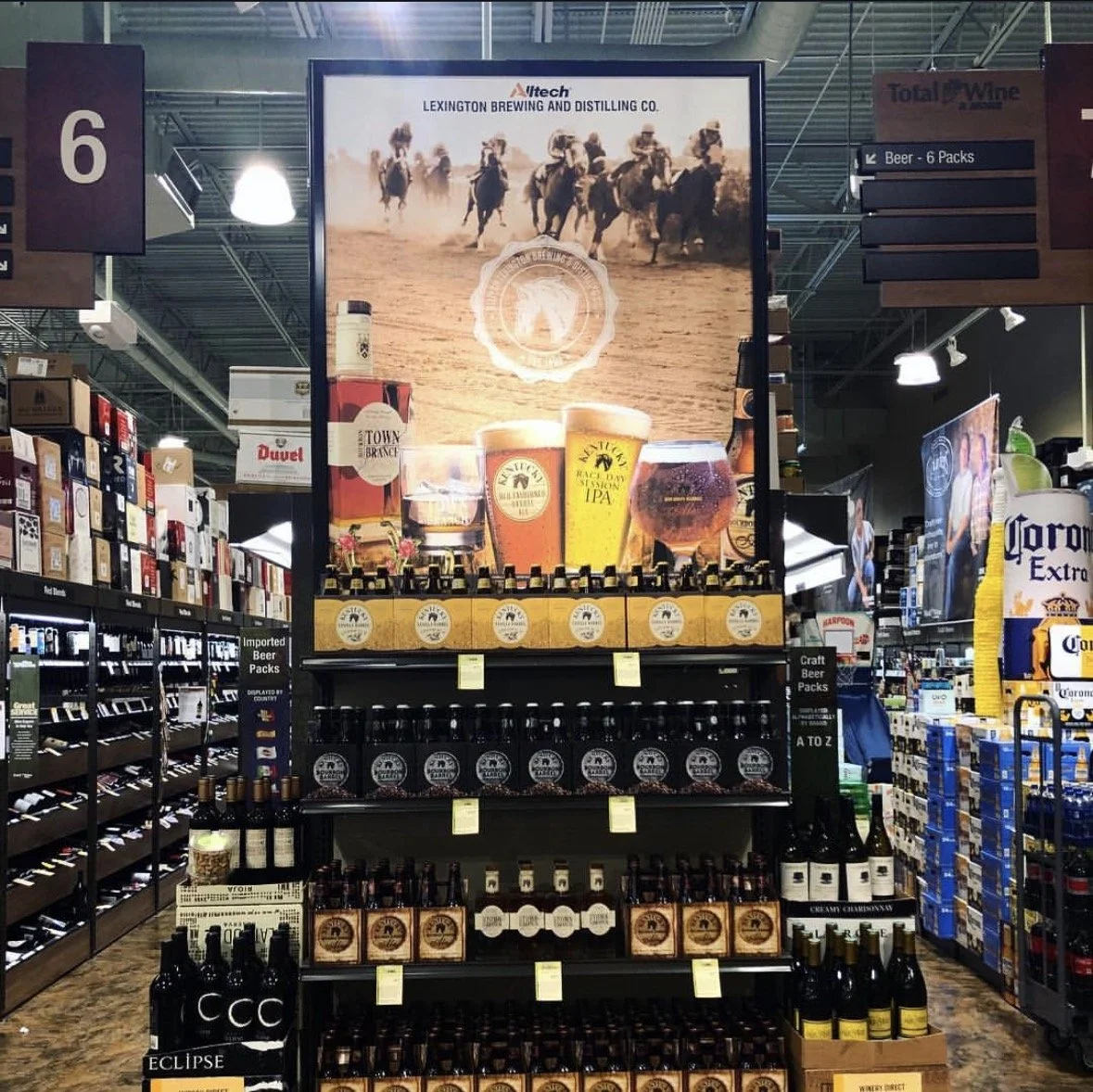 Display of various craft beers and IPAs at a liquor store, with a large promotional sign featuring horses running in a desert landscape and glasses of beer.