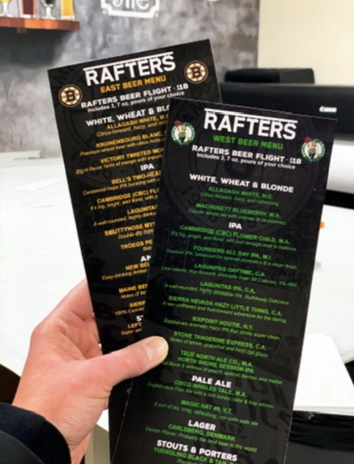 Two menus for Rafters, a bar or restaurant. One menu is titled East Beer Menu with yellow text, and the other is titled West Beer Menu with green text. Both menus list beer options and include small logos at the top.