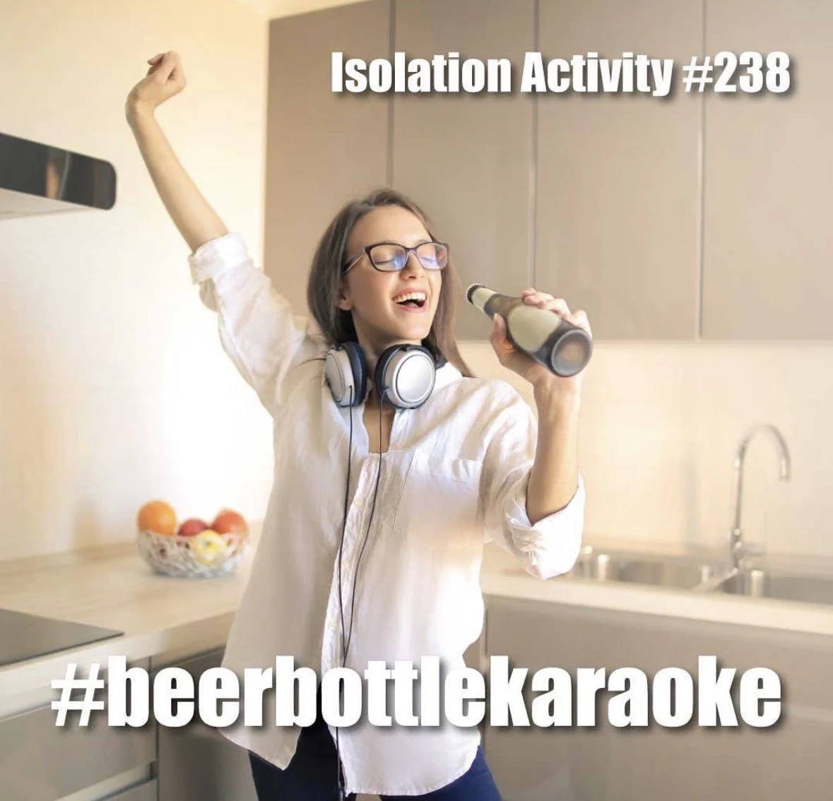 A woman singing with a beer bottle in a kitchen, wearing headphones and glasses, celebrating with one arm raised. The image has the text 'Isolation Activity #238' and '#beerbottlekaraoke'.