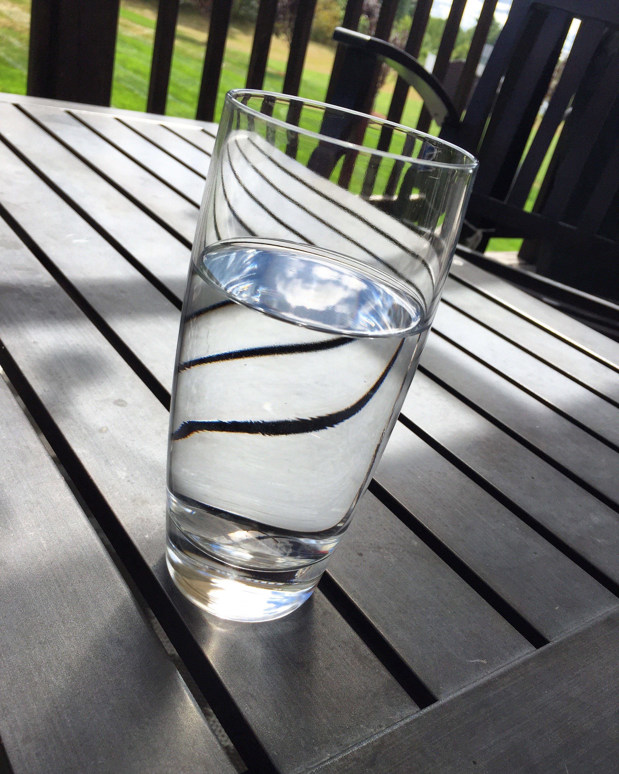 A clear glass of water on a wooden surface with a outdoor scene in the background.