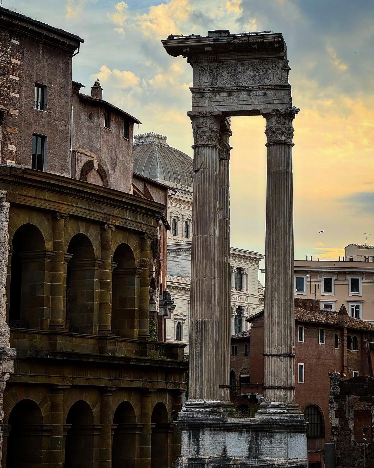 Ancient Roman columns and ruins in Rome, Italy, at sunset with a partly cloudy sky.