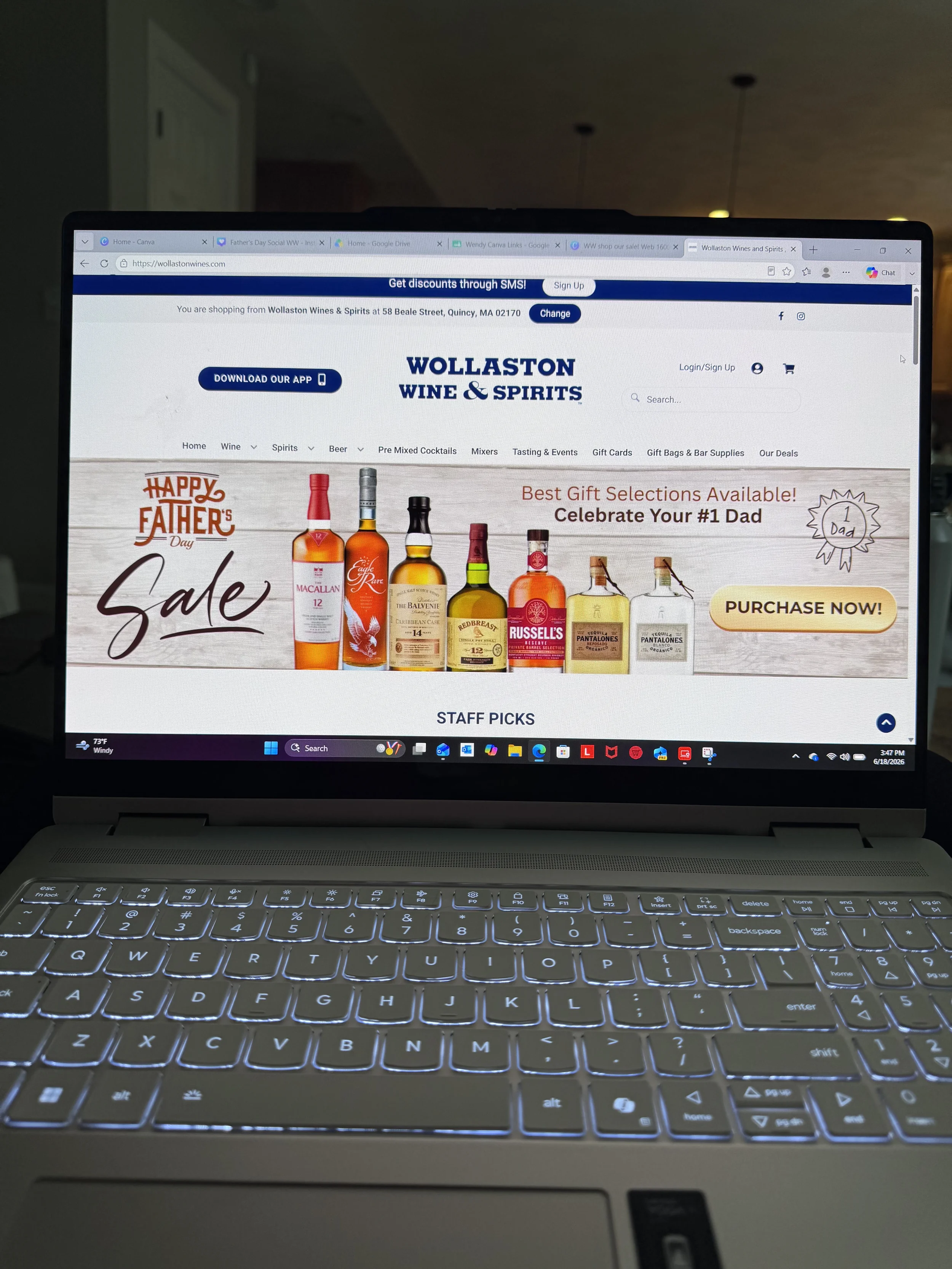 Laptop screen displaying an online wine store website with a Father's Day sale banner and various wine bottles for sale, including Macallan and Russell's.