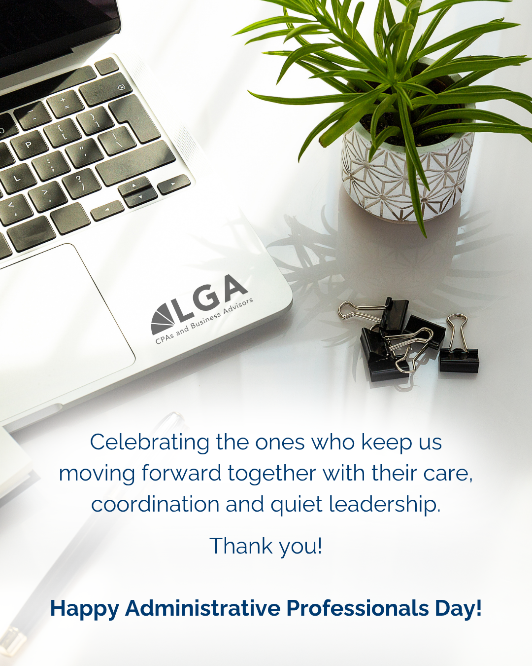 A laptop with an 'IGA CPAs and Business Advisors' sticker on a white desk, beside a potted plant and black binder clips, with a message celebrating Administrative Professionals Day.