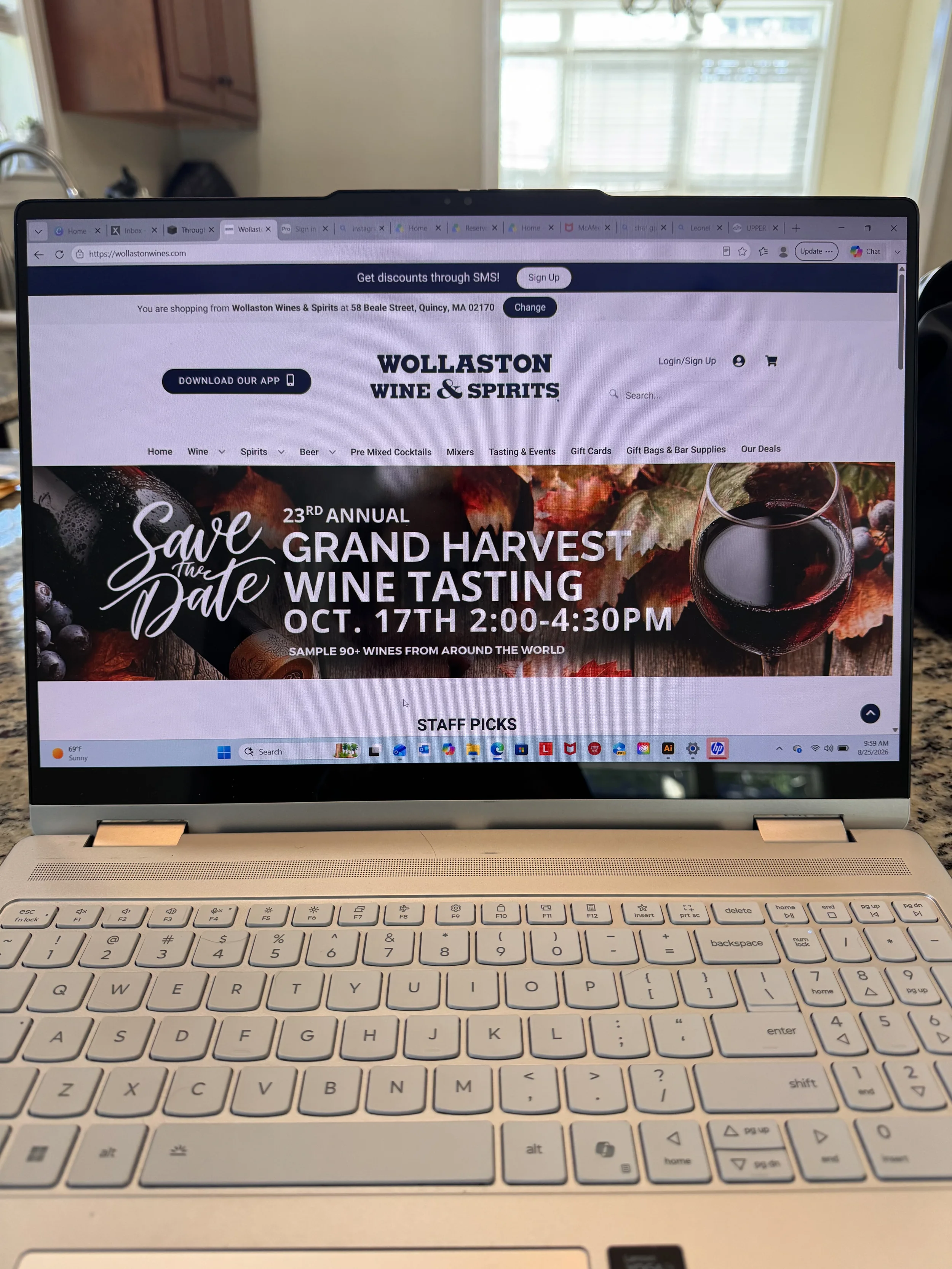 Laptop screen displaying a website for Wollaston Wines & Spirits with an event banner for a wine tasting event.