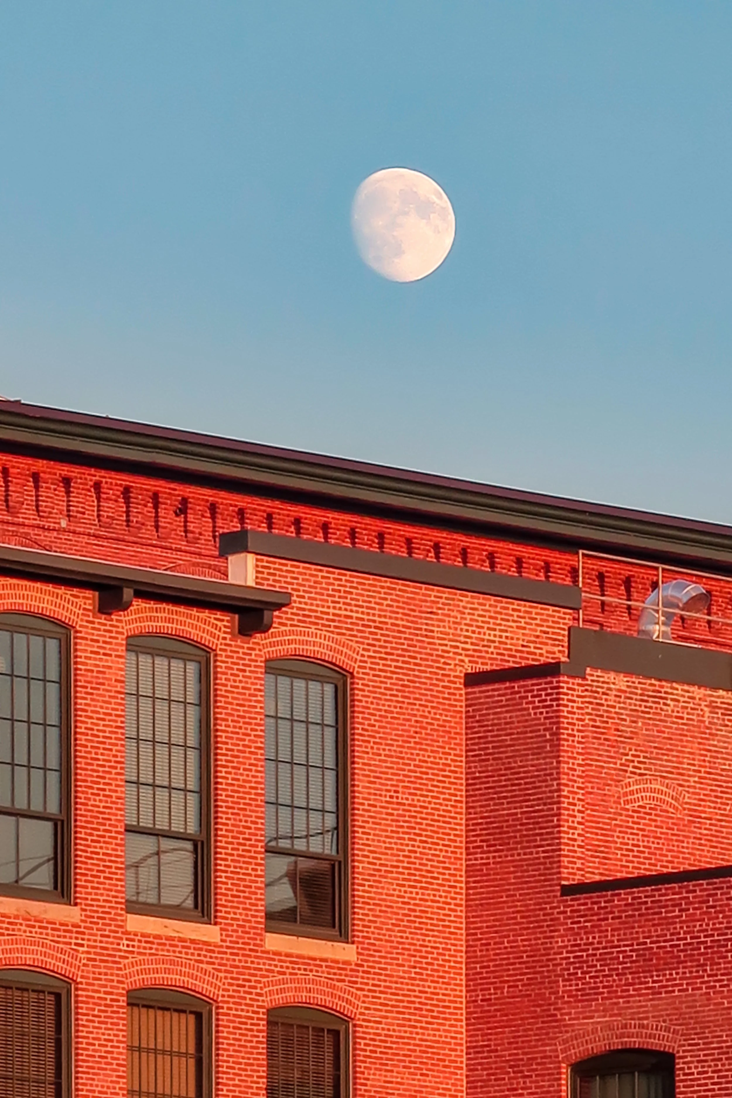 The moon is visible in the sky above a red brick building with multiple large windows.