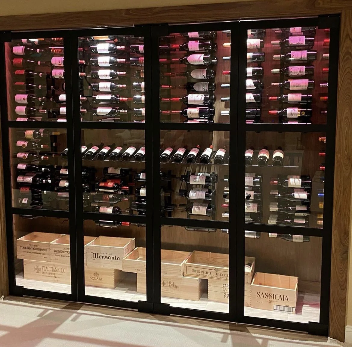 Wine bottles stored horizontally behind the glass doors of a walk in wine refrigerator.
