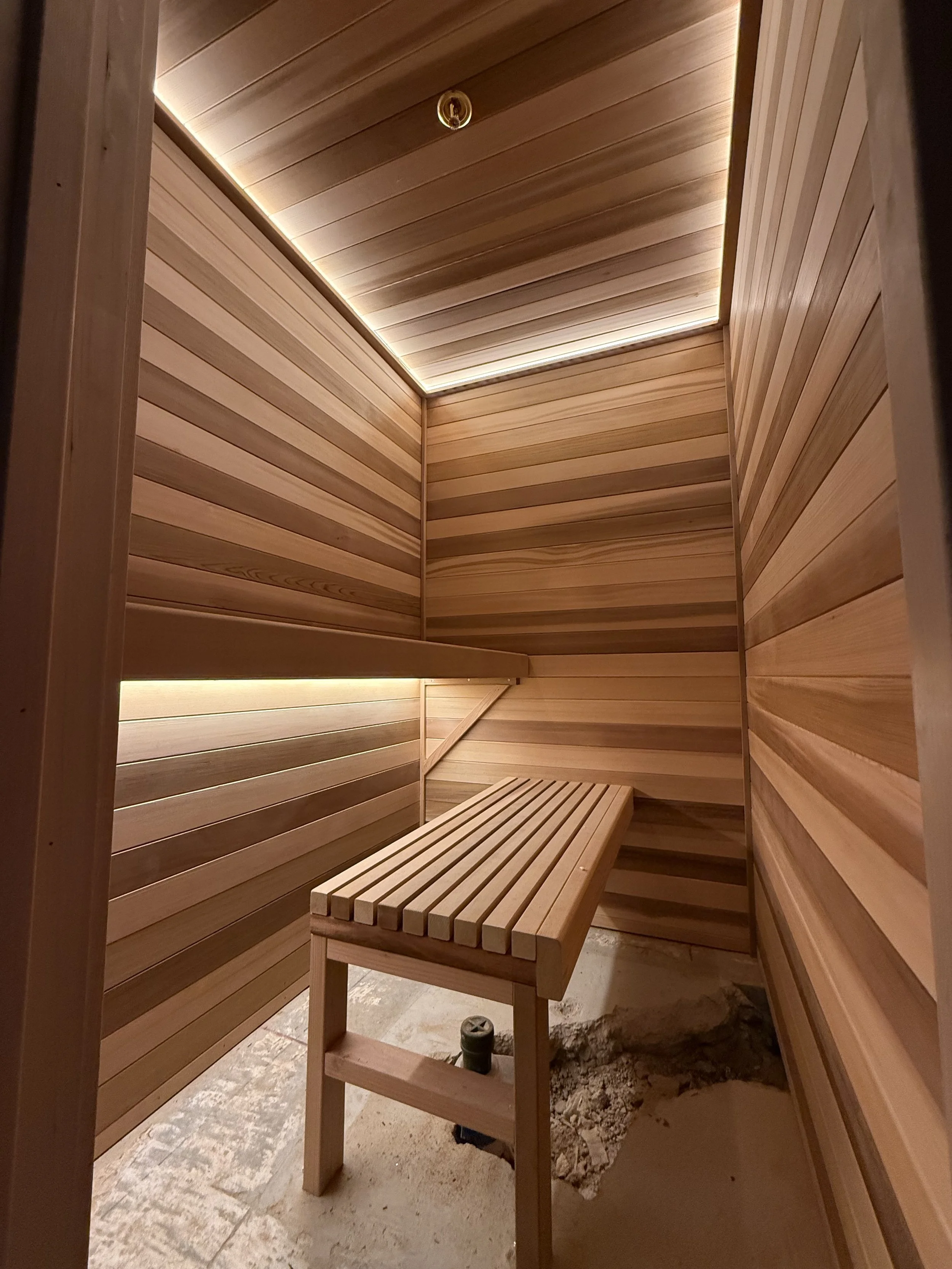 Wood-slat sauna under construction, walls and bench built with the floor not yet finished.