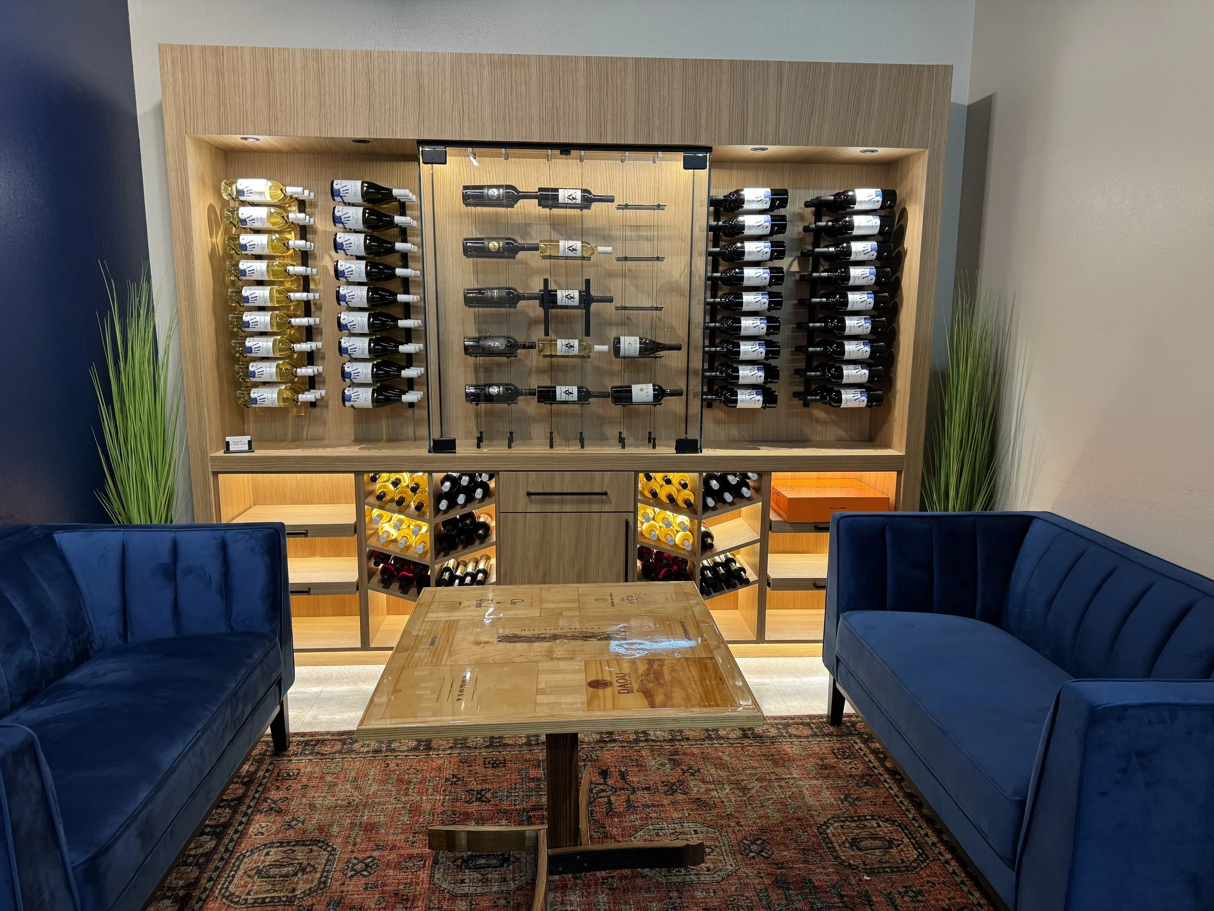 Wine display wall with a glass case and wood racking, flanked by two blue velvet sofas.