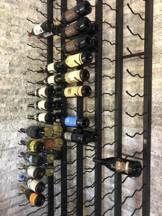 Wall-mounted metal wine rack holding rows of horizontally stored bottles.