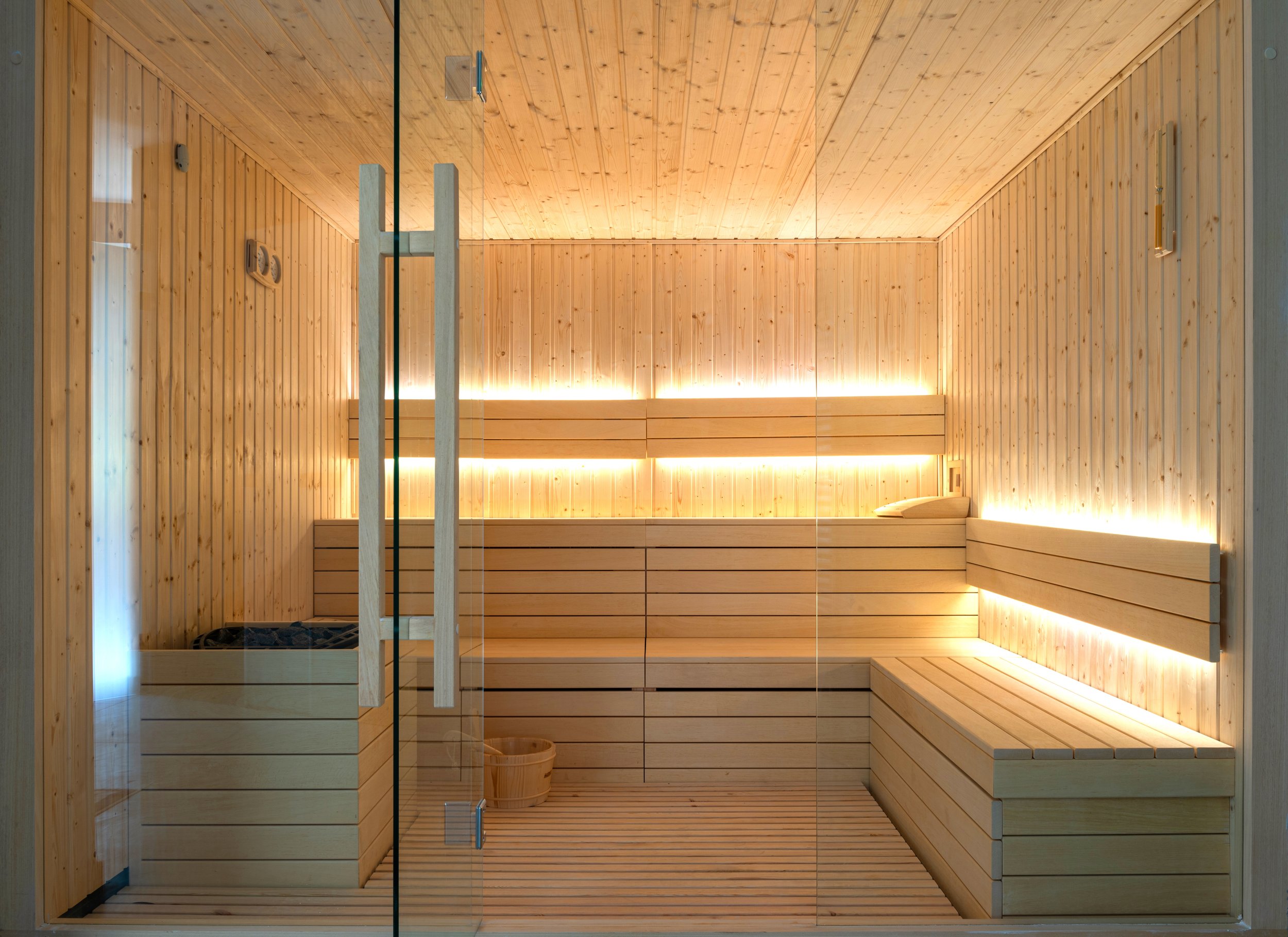 Wood-paneled sauna with built-in bench seating, a water bucket, and soft lighting.