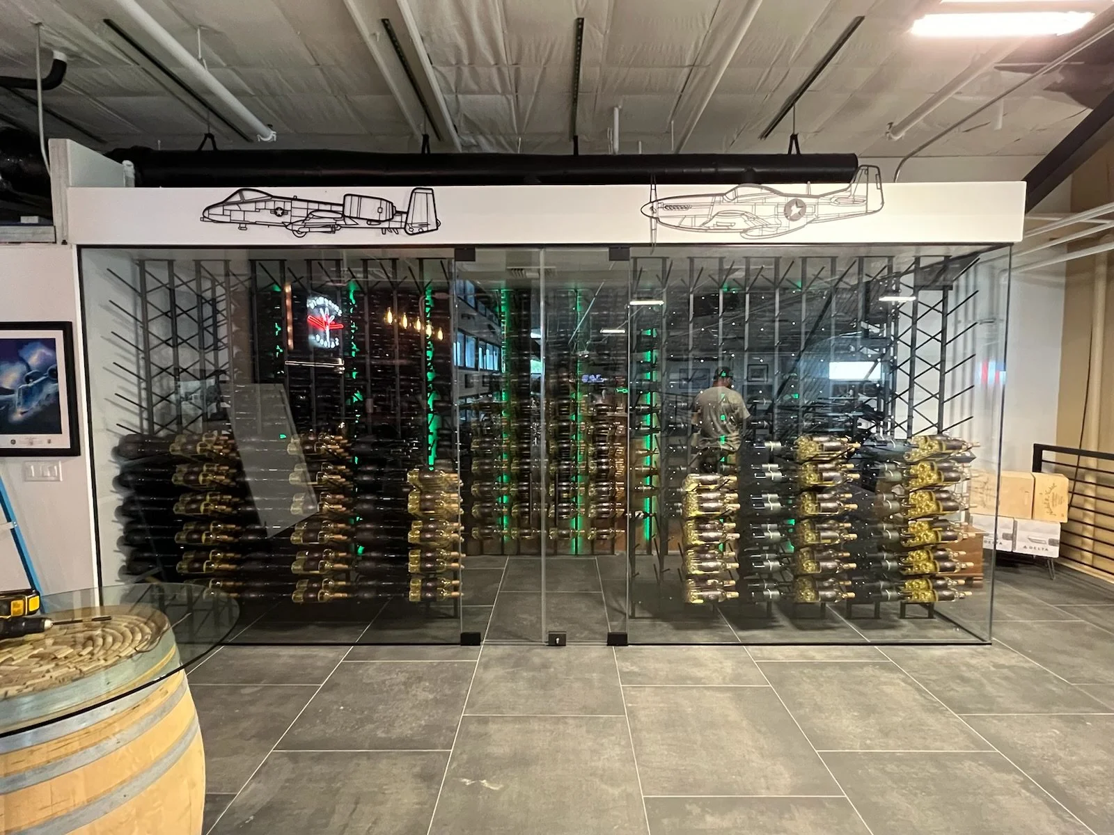 Wine bottles stored horizontally behind glass doors, with aircraft line drawings above the display.