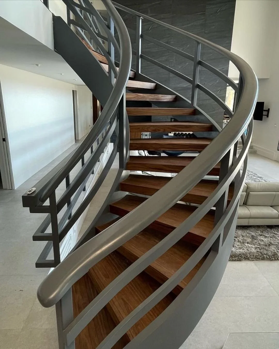 Floating spiral wood-tread staircase with gray metal railings in a bright living space.