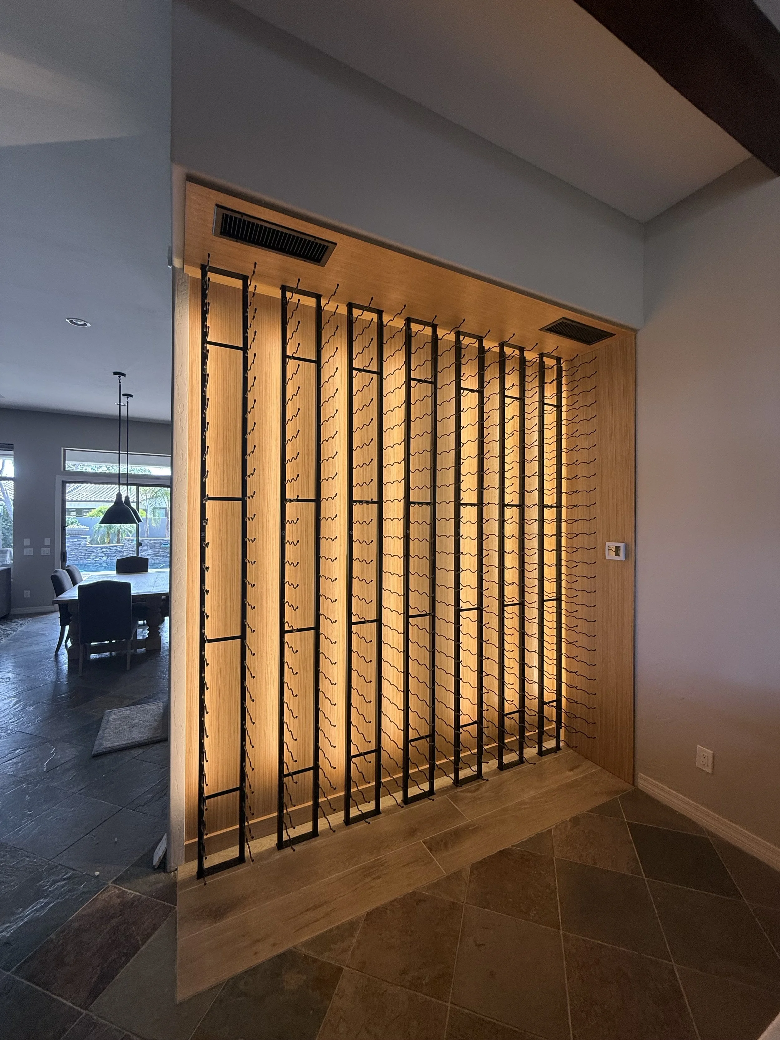 Wine display wall dividing a living and dining space, bottles racked on black metal.