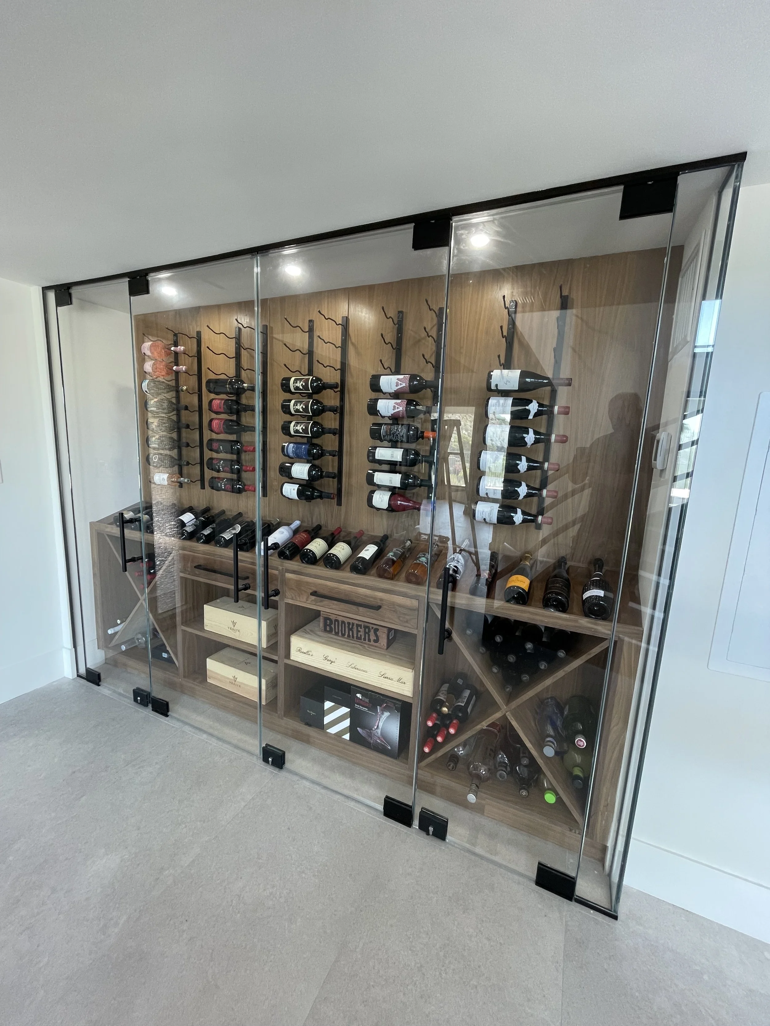 Glass-front wine storage cabinet filled with bottles in a carpeted room.