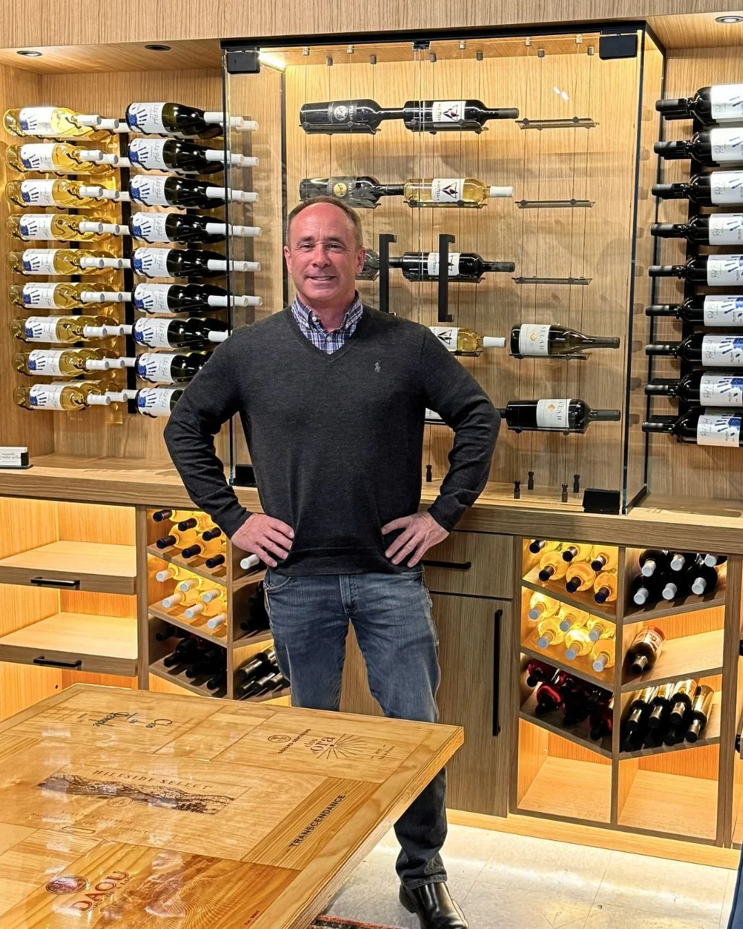 David James standing beside a custom built wine display wall with wood racking and a glass-front case for Barrett Jackson.