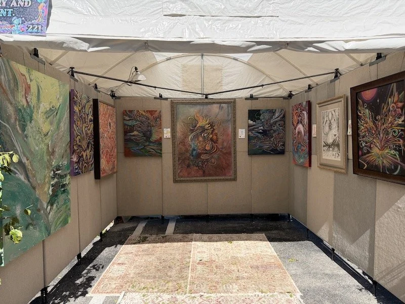 Art and typewriter poetry gallery display of colorful abstract paintings inside a beige tent at an outdoor event.