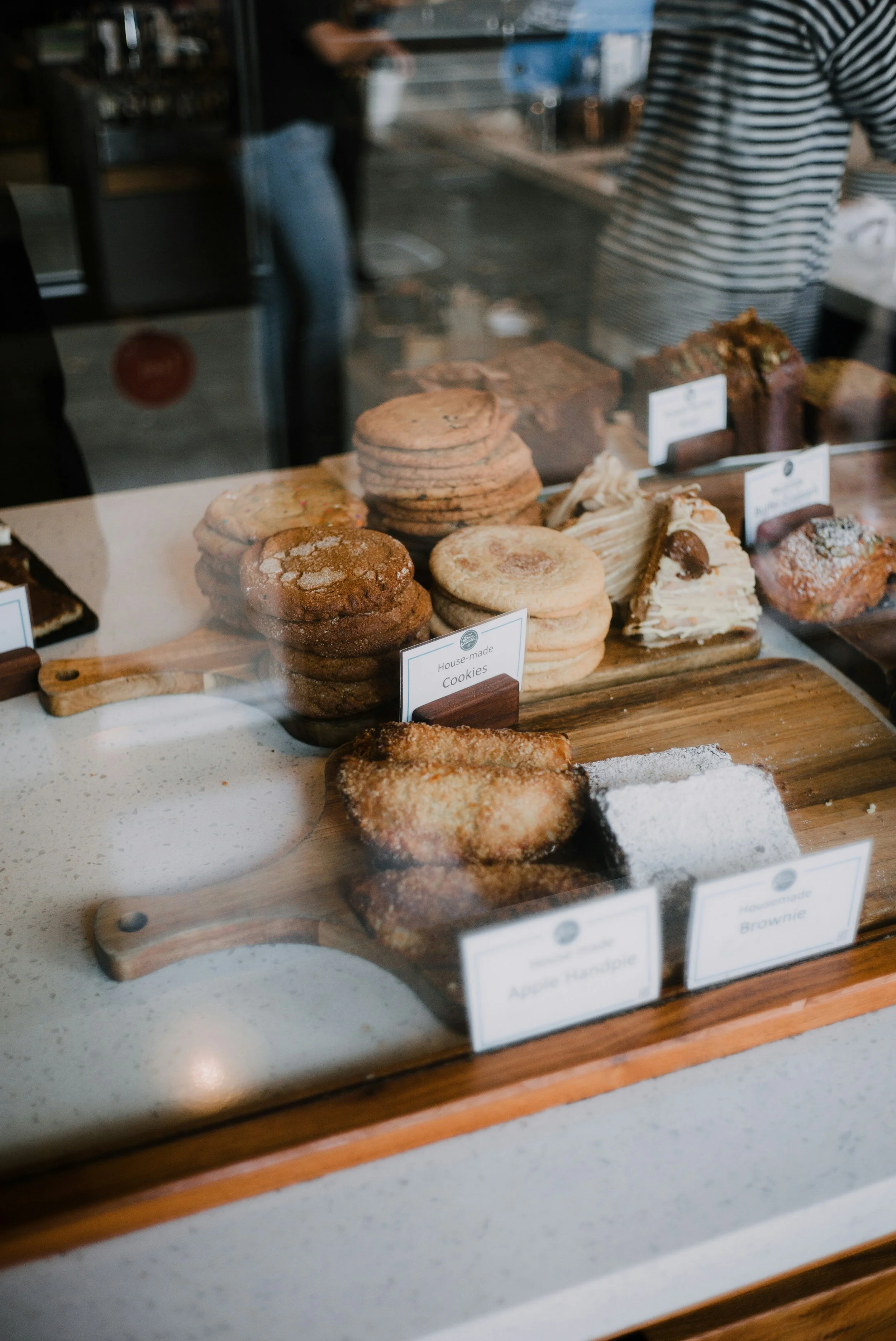 Display of assorted baked goods including cookies, apple handpie, and brownie behind glass at a bakery.