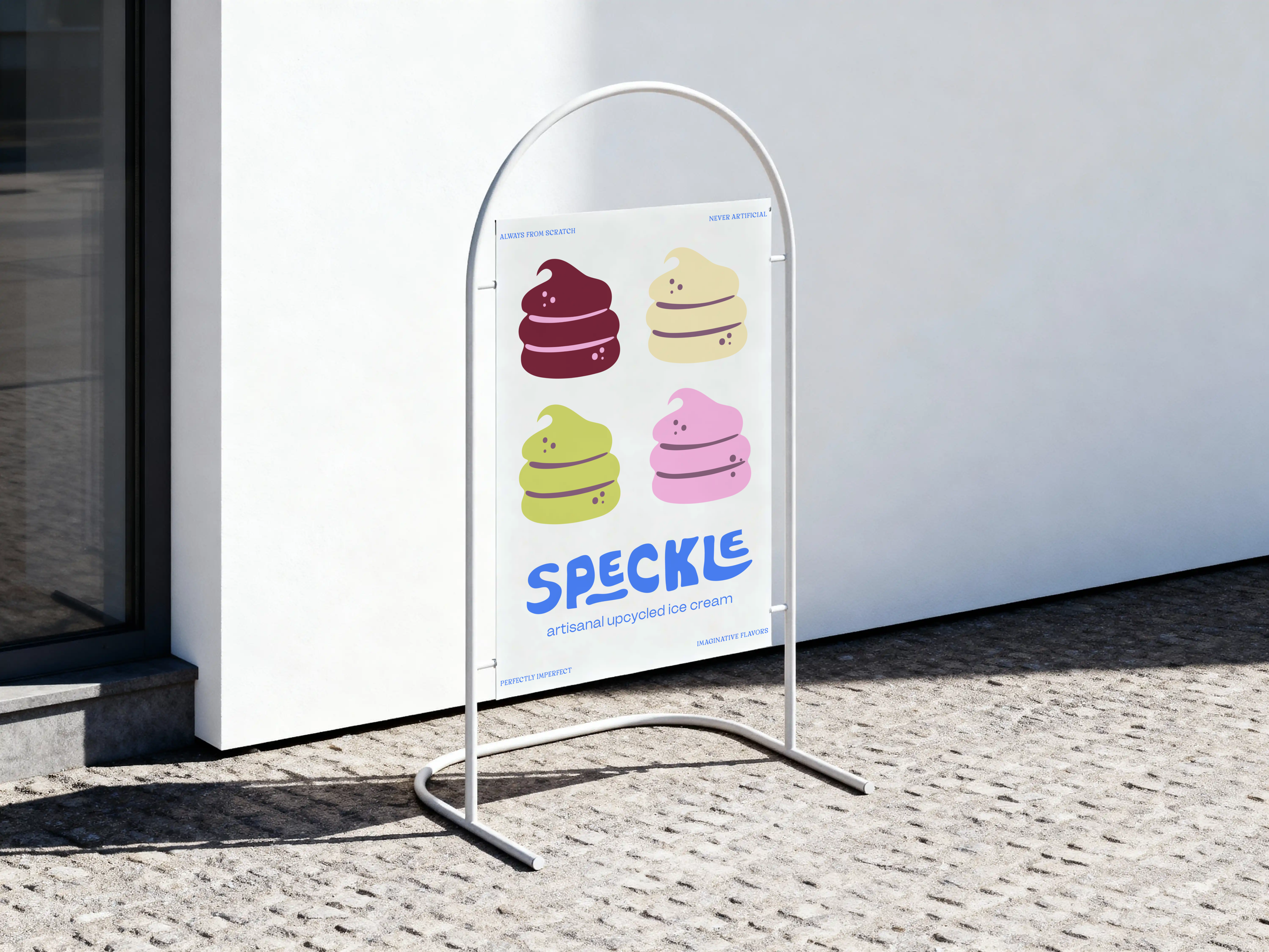 A white sandwich board sign outside a building displaying colorful illustrations of soft-serve ice cream cones in purple, yellow, green, and pink, with the text 'SPECKLE' and 'artisanal upcycled ice cream' below the graphics.