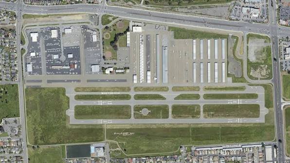 An aerial view of an airport runway and taxiways surrounded by buildings and green areas.