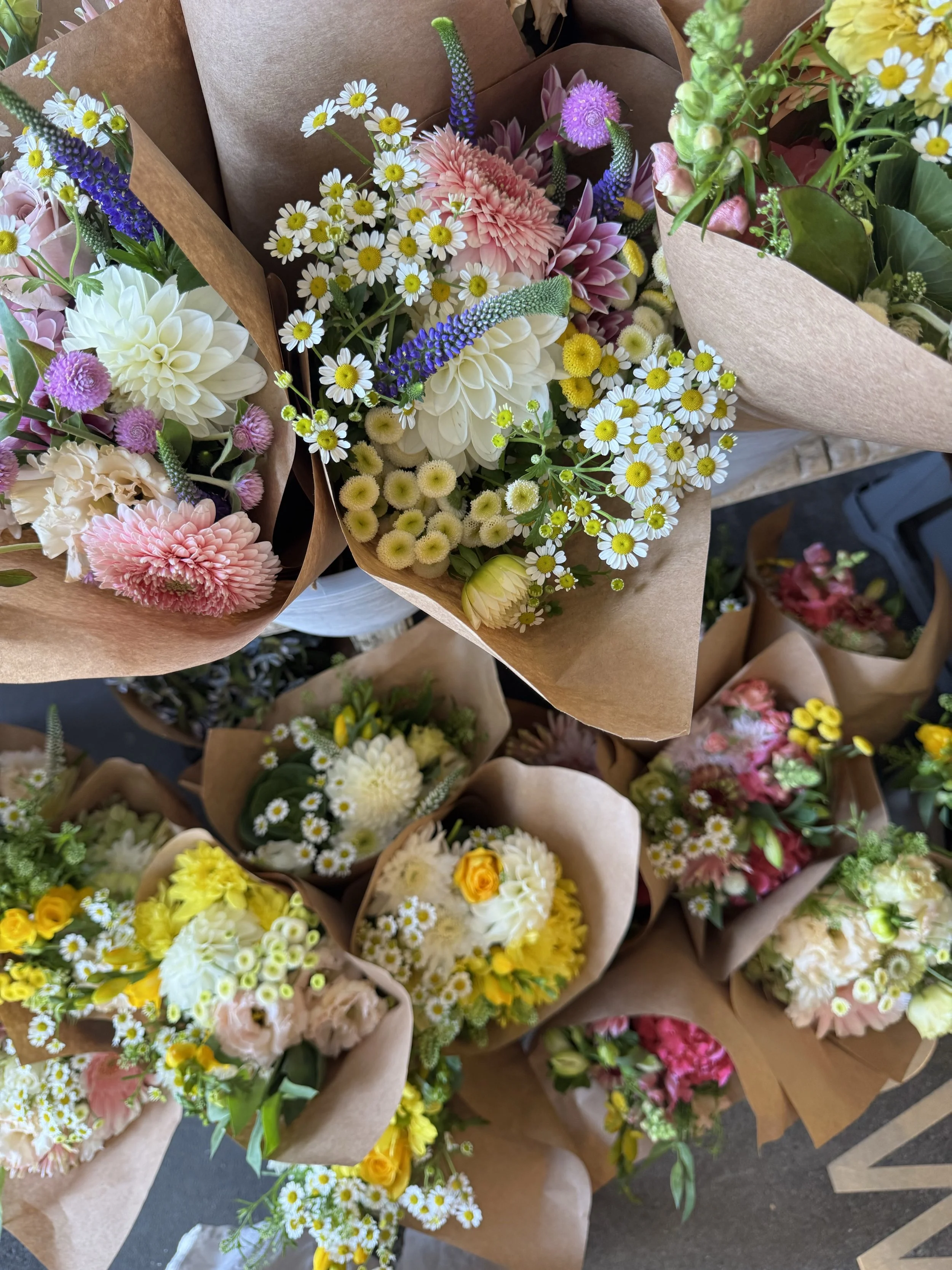 Various colorful flower bouquets wrapped in brown paper on a display table.