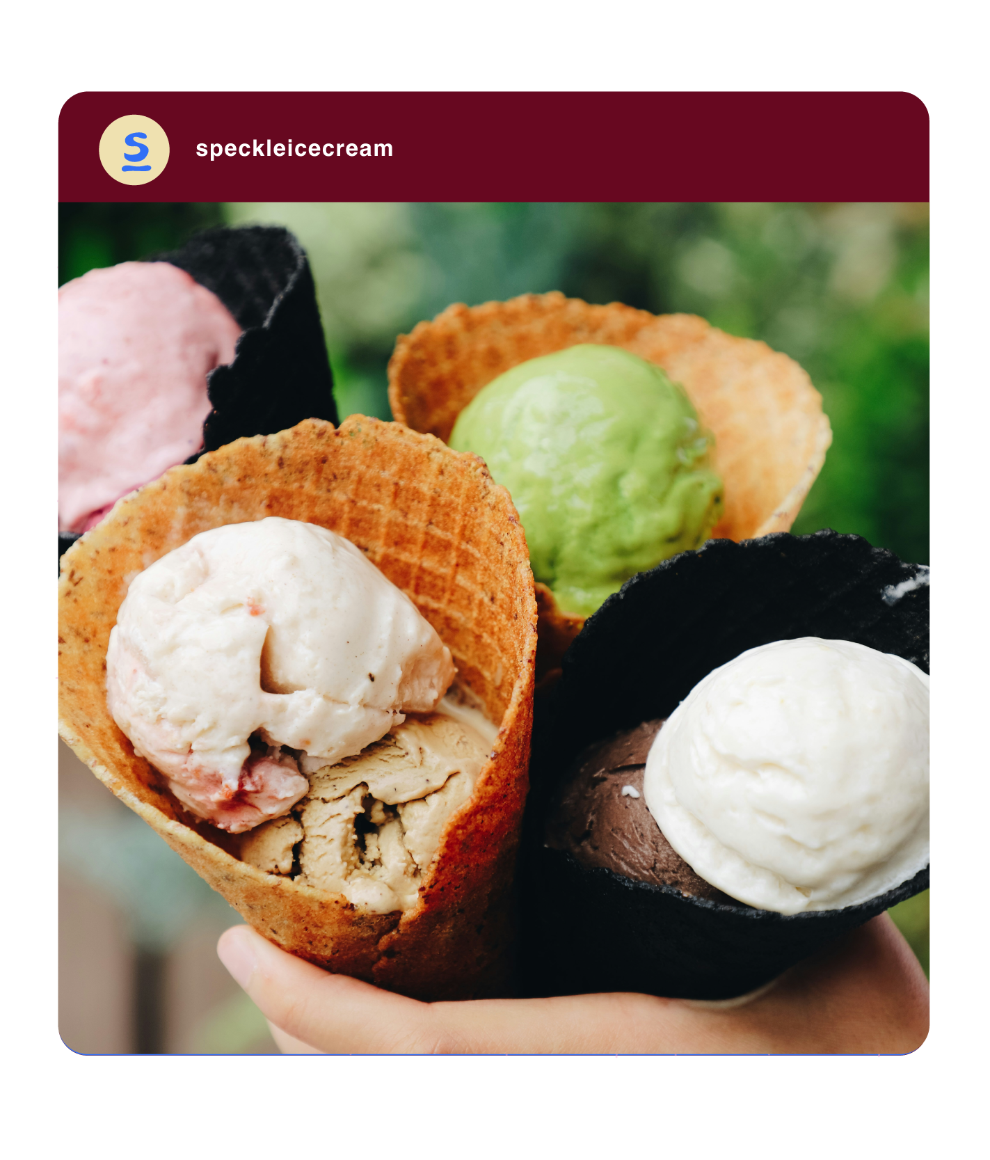 Close-up of two ice cream cone cups, one with vanilla and chocolate ice cream, and the other with green, black, and pink ice creams, held outdoors with a blurred green background.