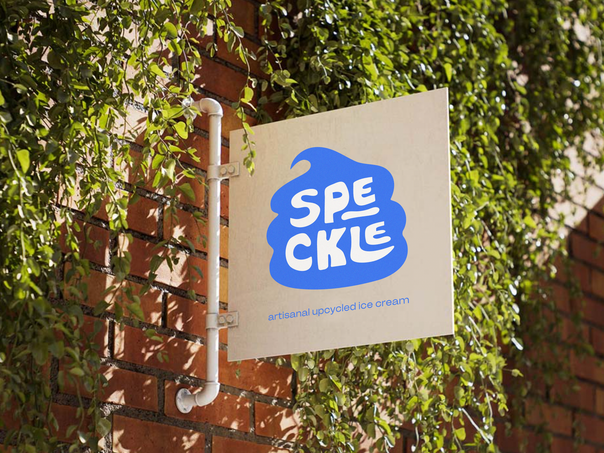 A sign reading 'SPECKLE,' attached to a white pipe, extends from a brick wall covered in green ivy, with sunlight casting shadows on the scene.