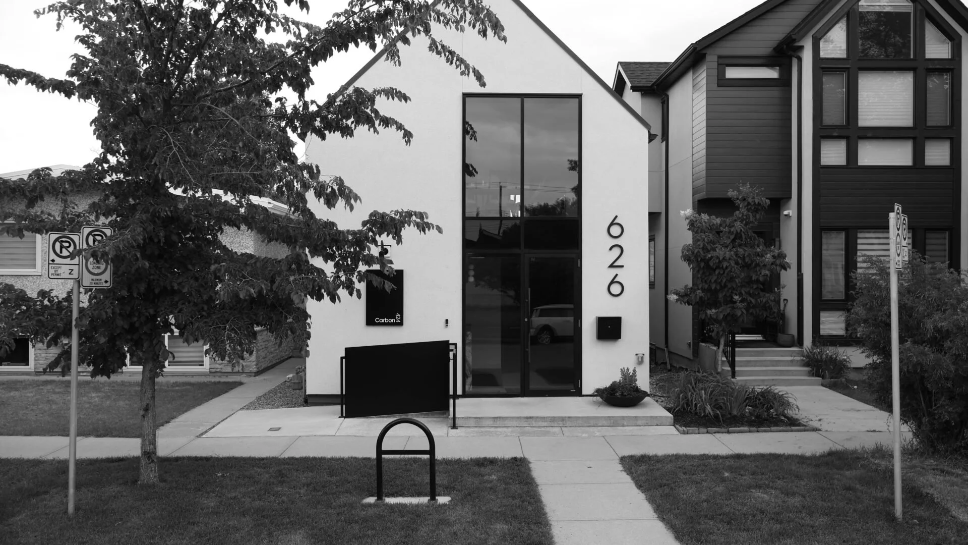 Our Carbon 424 location, a modern residential building with the house number 626 on the front, large glass windows, and front entrance with steps and plants, on a neatly landscaped lot with trees and a sidewalk.