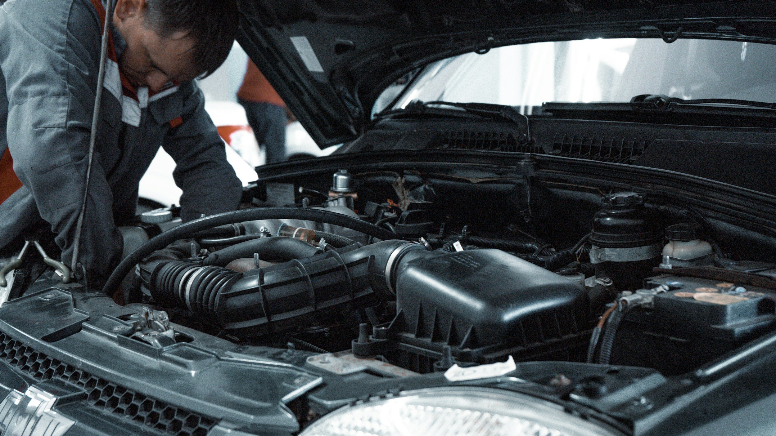 A mechanic working under the hood of a car while inspecting the engine in a garage.