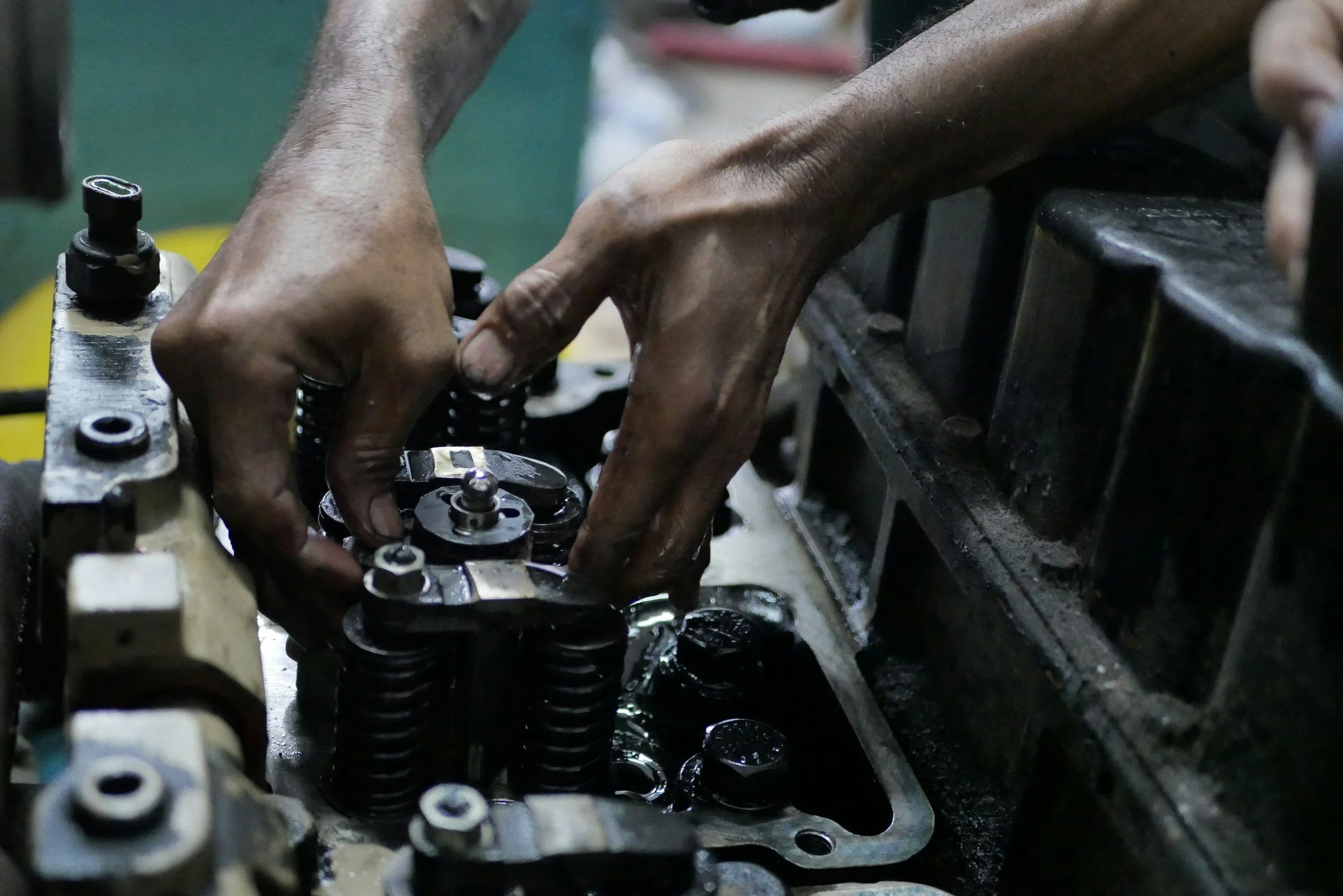 Close-up of a mechanic's hands working on an internal engine component, with visible springs and metal parts.