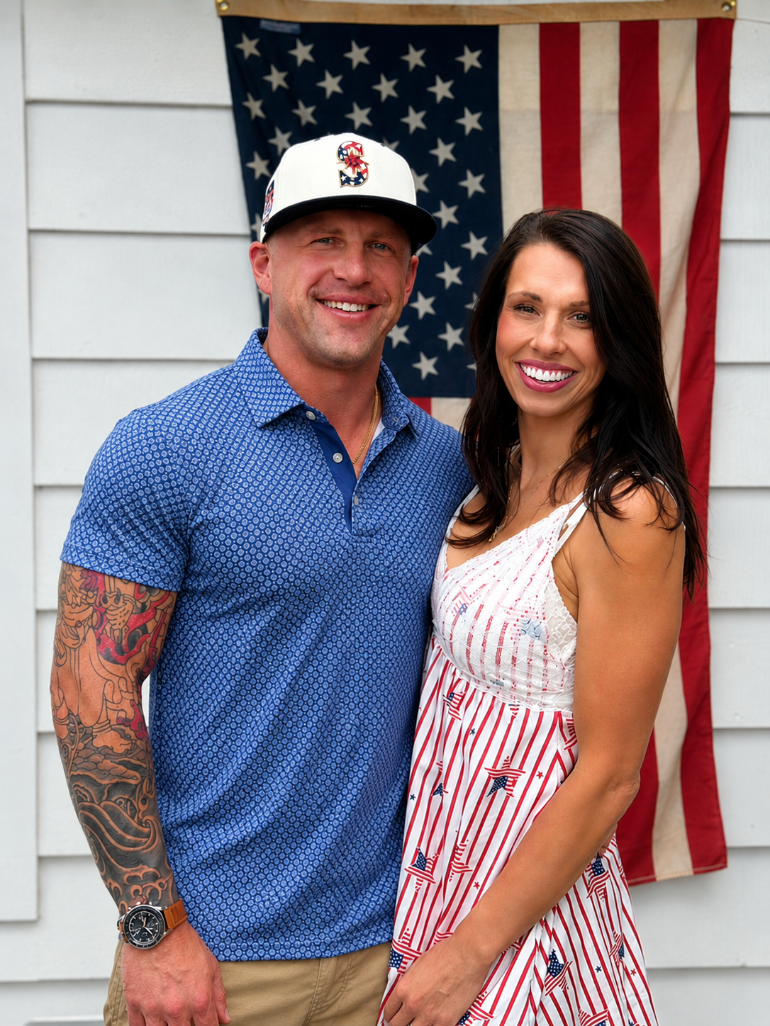 A smiling man and woman standing outdoors in front of an American flag, dressed in patriotic clothing suitable for a patriotic celebration.