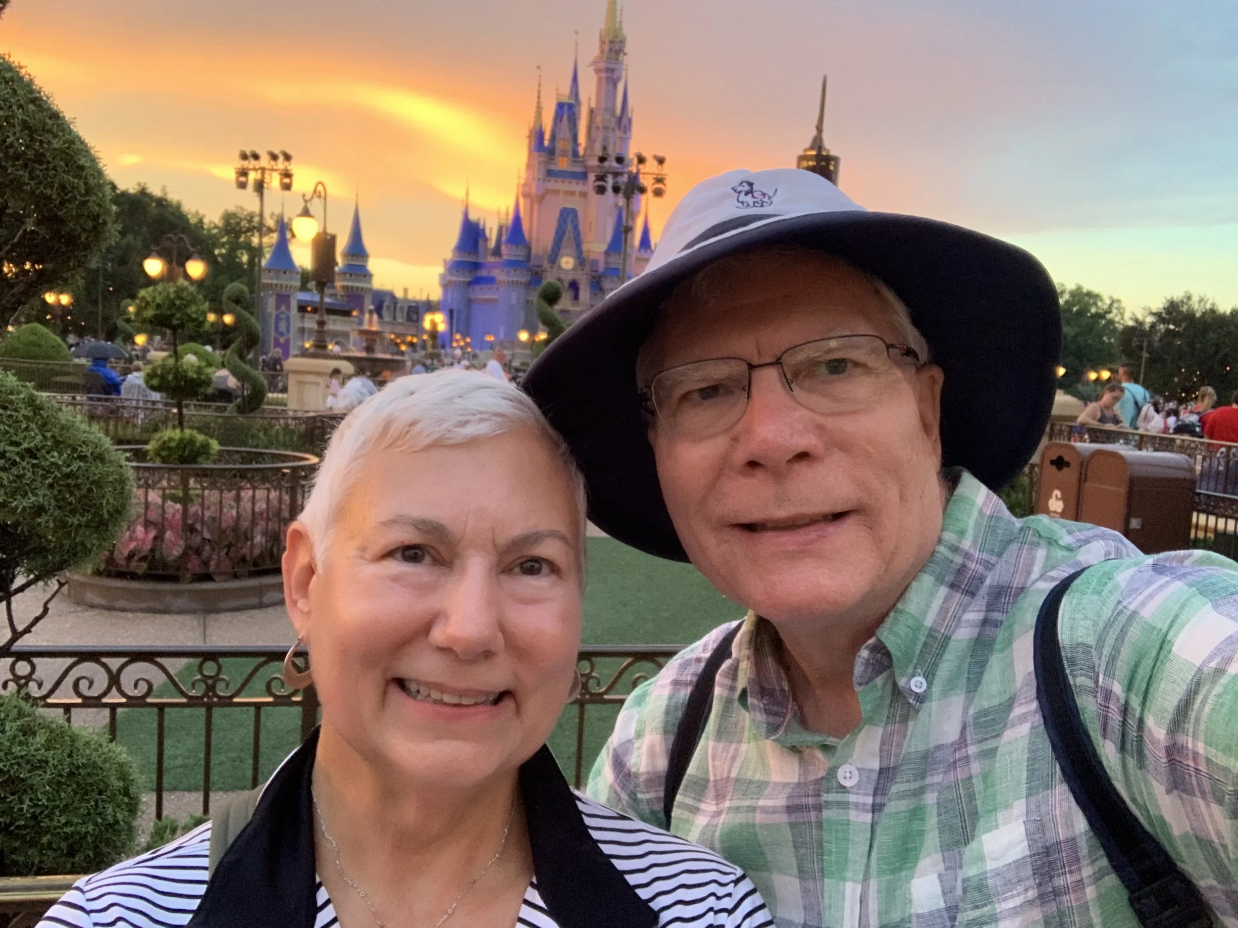 A man and woman taking a selfie at Disneyland, with Sleeping Beauty Castle in the background, during sunset.