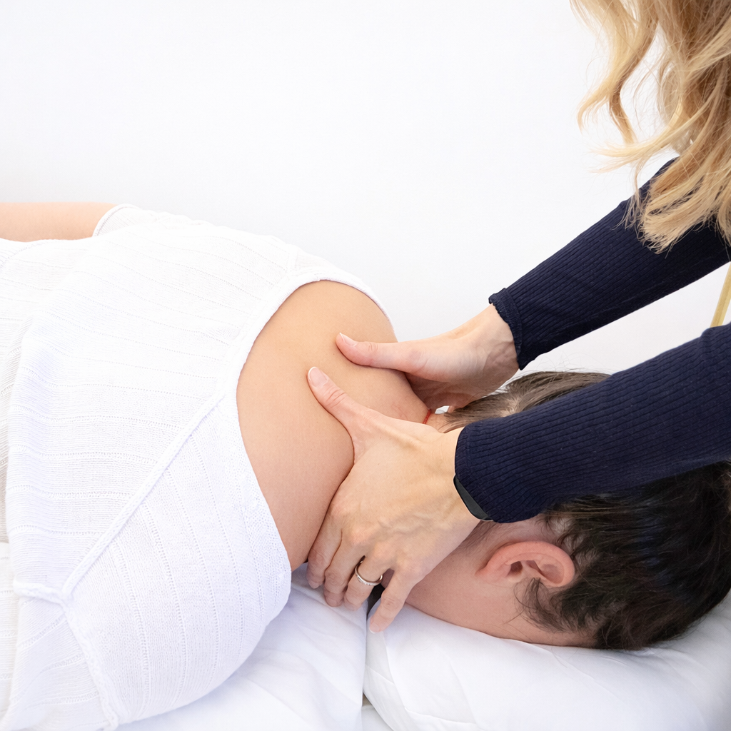 A person lying face down on a bed receiving a massage on their shoulder and neck area from a massage therapist.