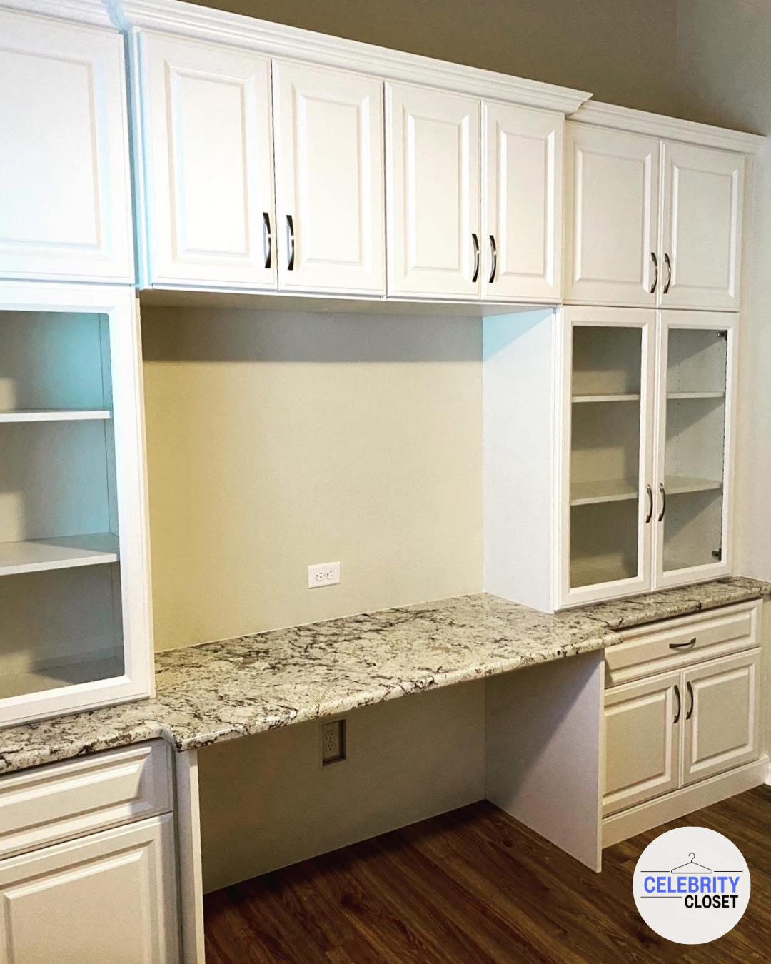 Empty kitchen cabinet with white upper and lower cabinets, granite countertop, and hardwood floor.