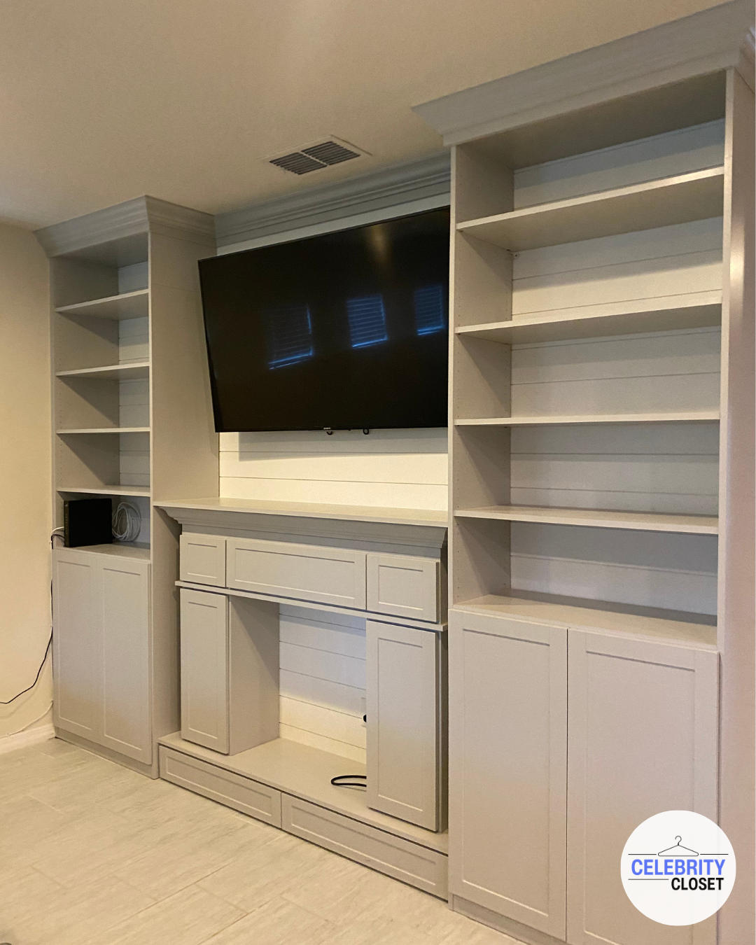 White built-in entertainment center with open shelves and storage cabinets surrounding a wall-mounted flat-screen TV.