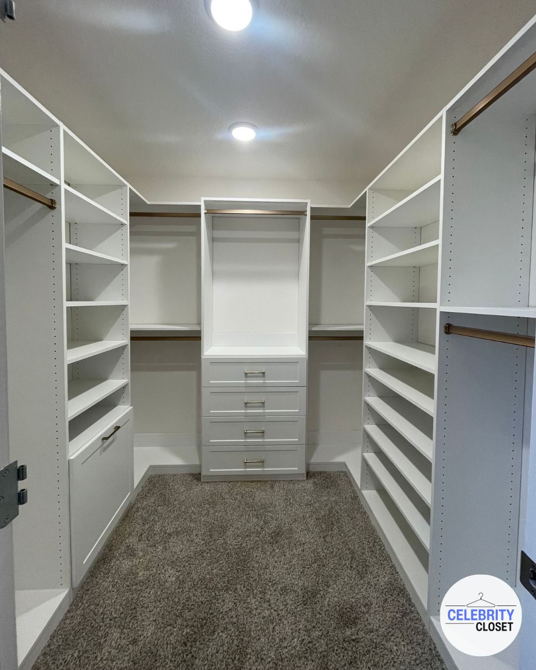 Empty walk-in closet with white built-in shelves and drawers, brown hanging rods, and beige carpet.