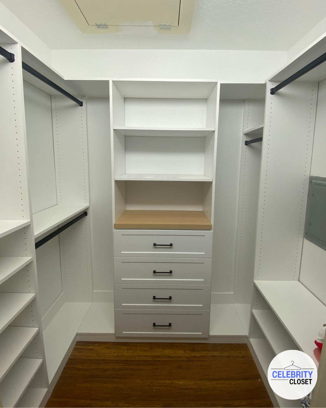 Empty walk-in closet with white shelving and drawers, black handles, and wood flooring.