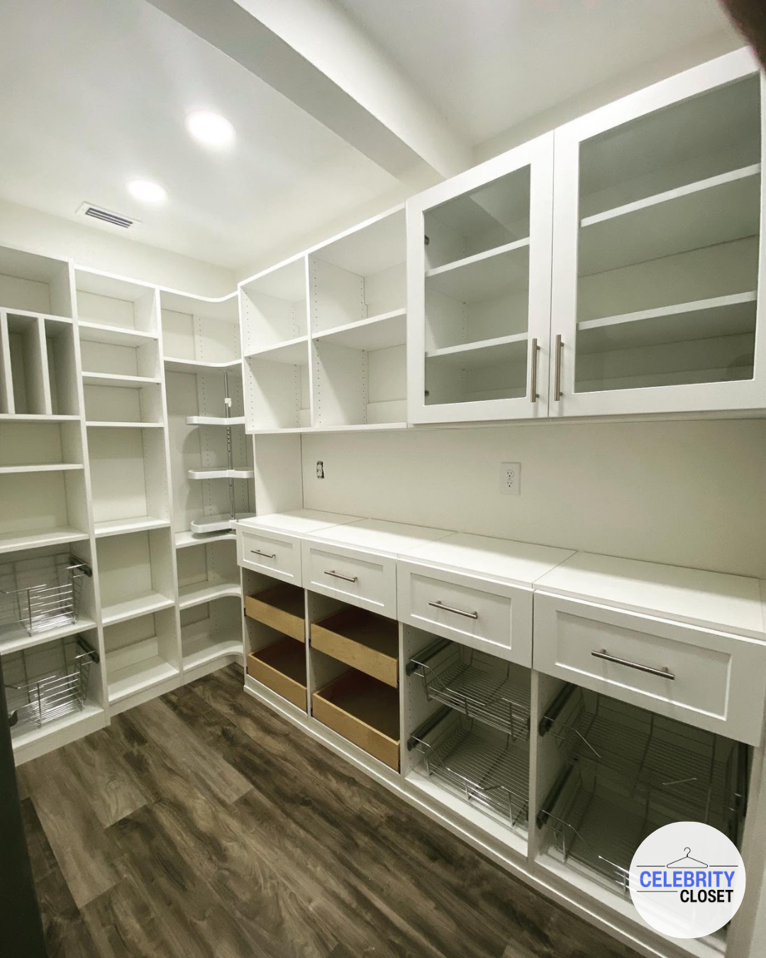 An empty walk-in closet with white shelving, drawers, and cabinets, and wood-like flooring.