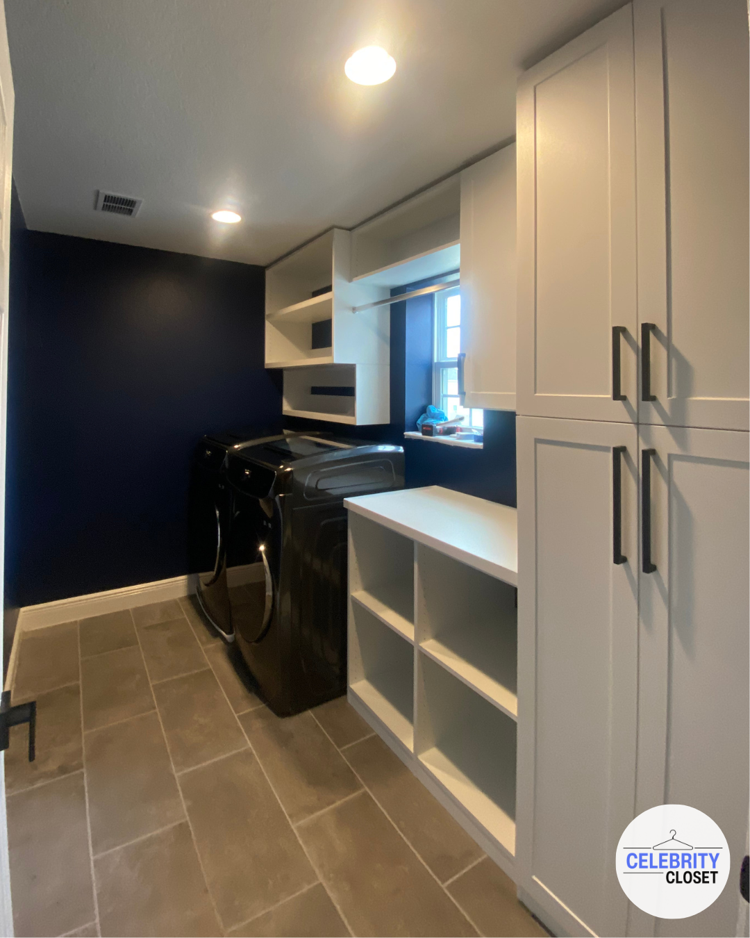Laundry room with white cabinets, a window, and a black washer and dryer set.