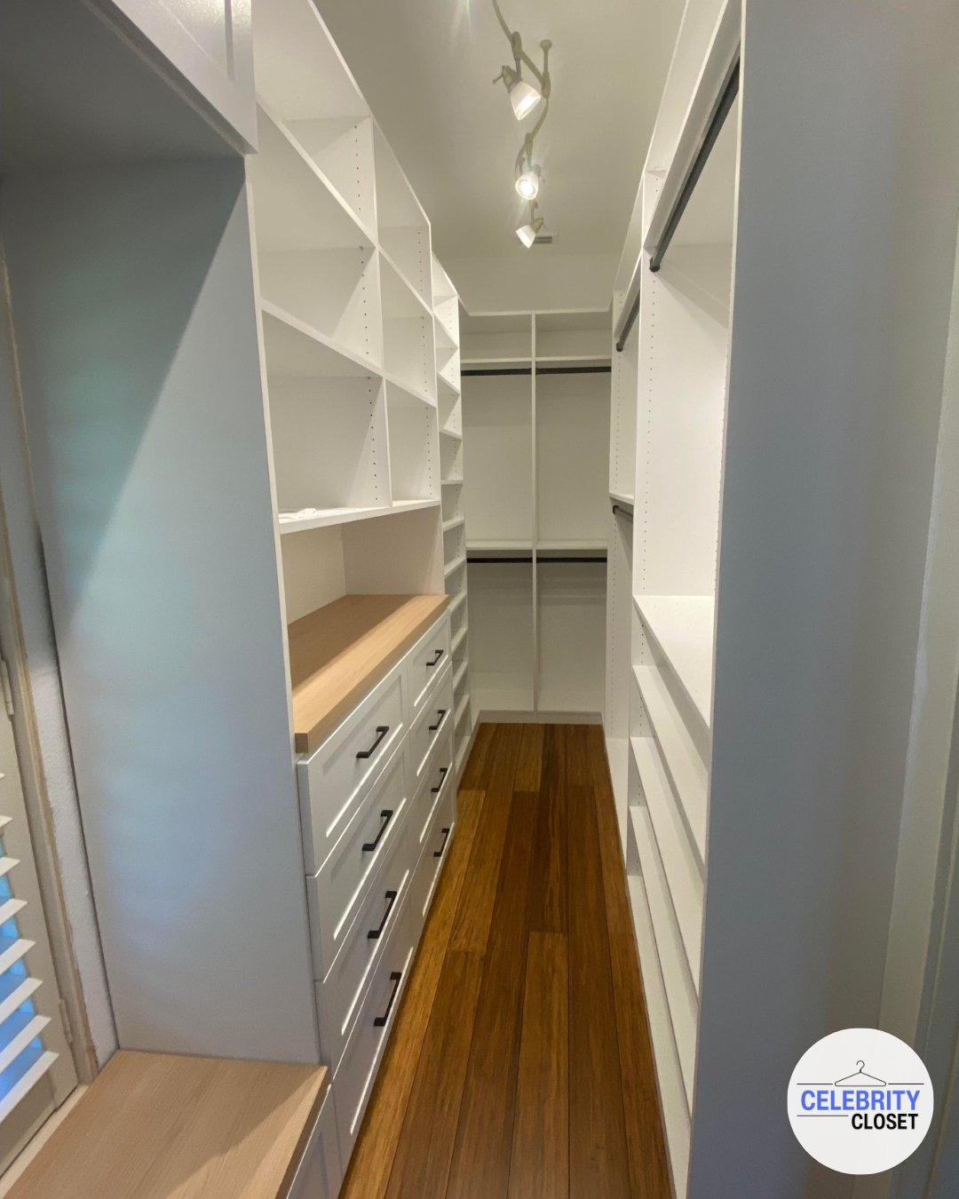 Empty walk-in closet with white shelving and drawers, wooden countertop, and hardwood floors.