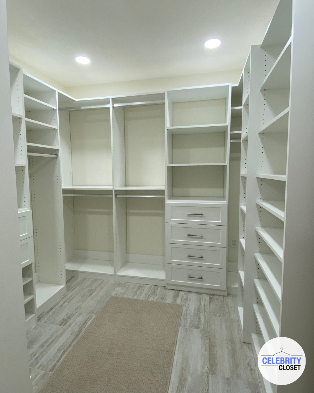 Empty white walk-in closet with built-in shelves, drawers, and hanging rods, illuminated by ceiling lights.